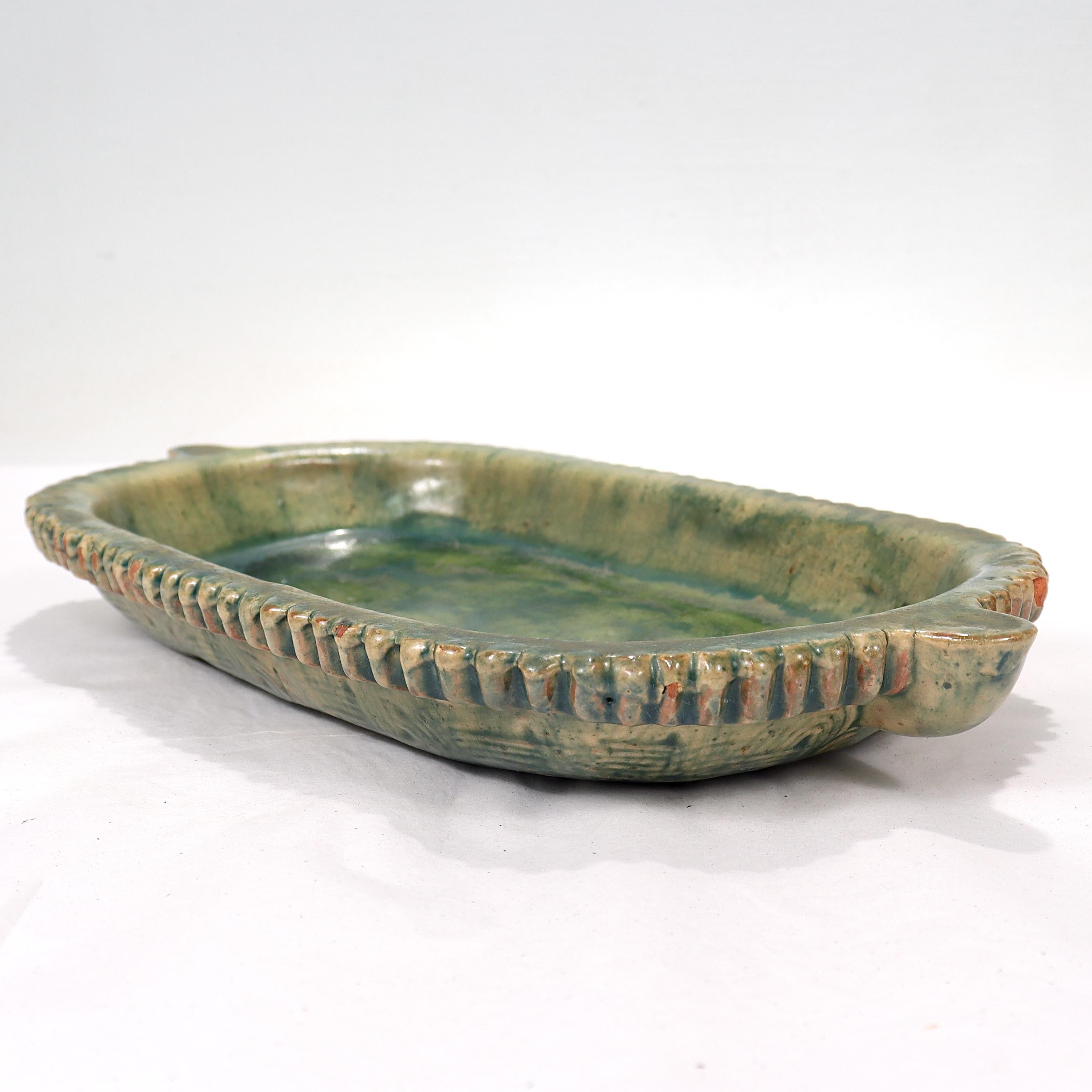 A fine, rare, American Arts & Crafts pottery low bowl or oblong plate.

In the form of a long oblong bowl or plate with protruding handles at either end. There is cracklature throughout that gives it an aged look.

The underside of the bowl is