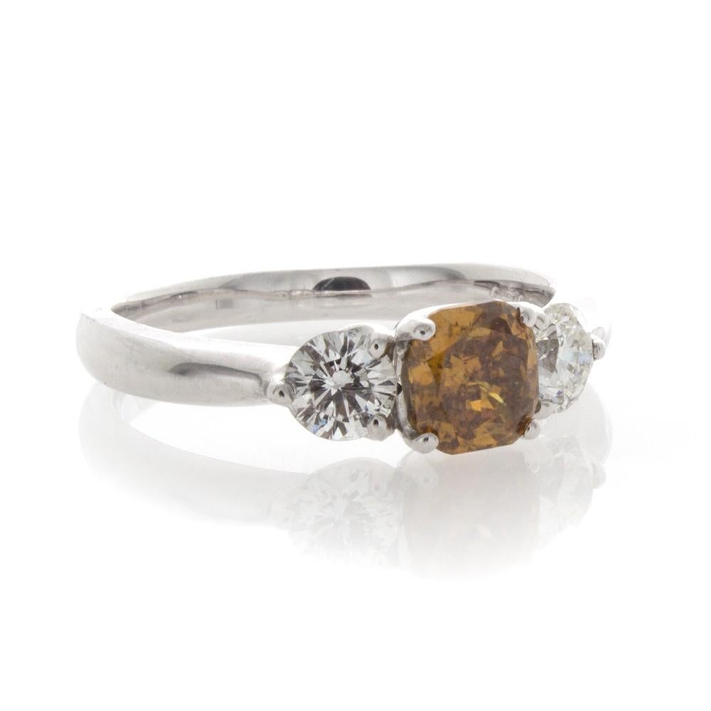 The Platinum ring has a .54 Carat Cushion cut Natural Fancy Color Diamond at the center.  This Diamond is Orangey Brown in color, and is SI2 Clarity.  A very vibrant and bright Diamond!  Accenting this are two .35 Carats each White Diamonds, H
