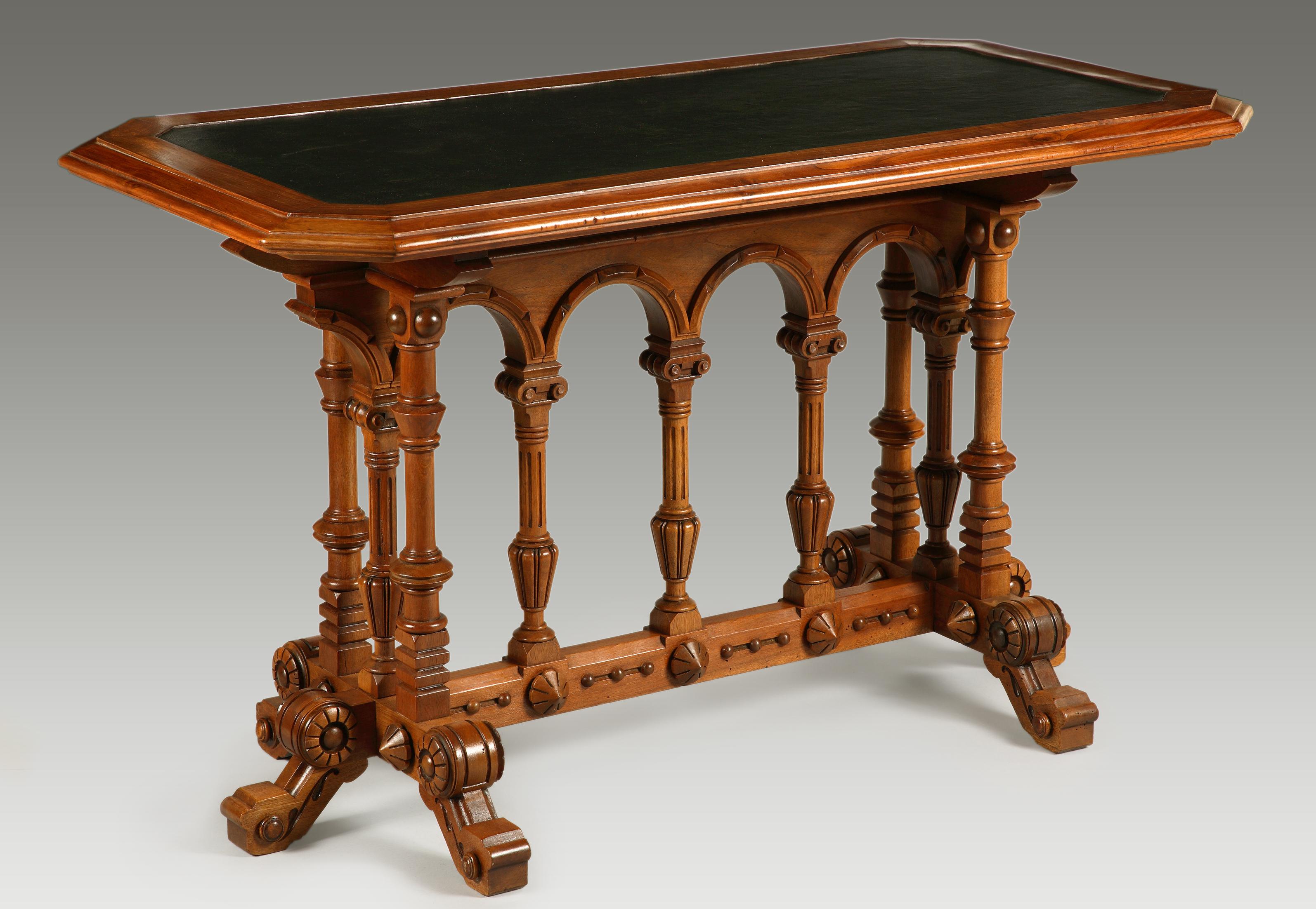 Carved wood table with Renaissance style motifs. Raised on six legs joined by a stretcher, with architectural decoration of ionic columns and blind arches. Top with leather inset writing surface.