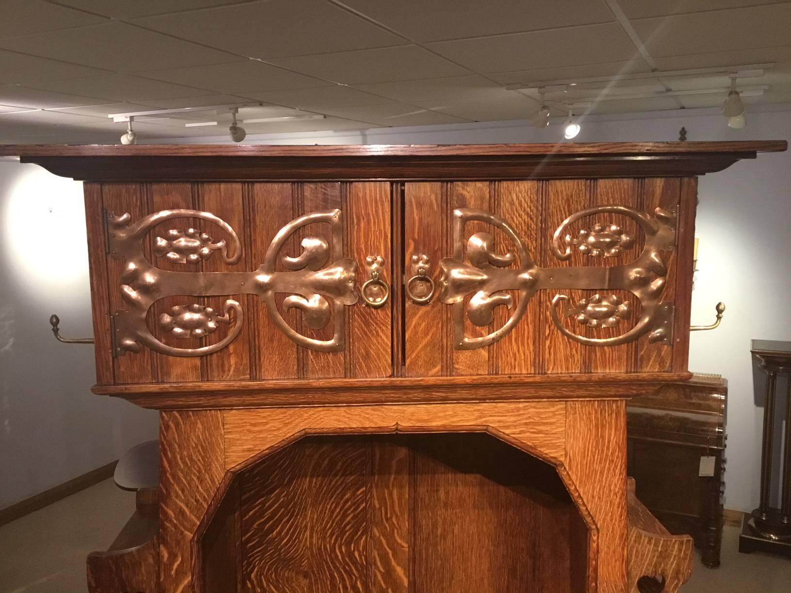 A rare oak Arts & Crafts period hall robe by Shapland & Petter of Barnstaple. Having a flared oak cornice above rectangular oak doors with fine hand beaten copper strap work hinges and handles. The doors open to reveal storage. The open front in