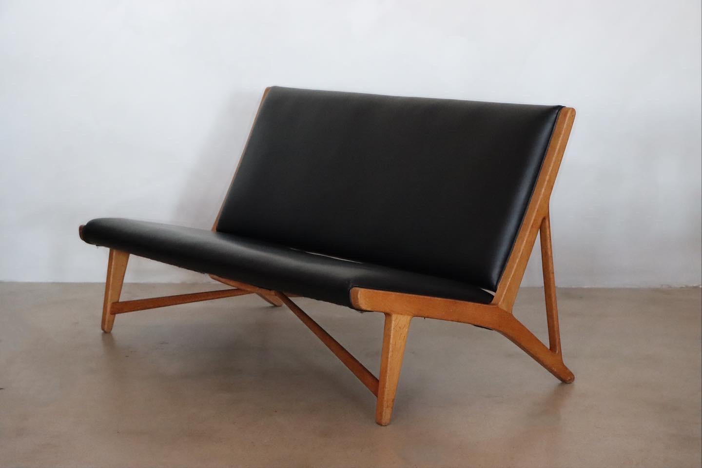 Rare and early “JH 555” armless sofa designed by Hans J. Wegner for Johannes Hansen, c. 1950s. Executed in oak and has been restored in soft black leather. These early examples were hand crafted in Johannes Hansens workshop and was produced in very