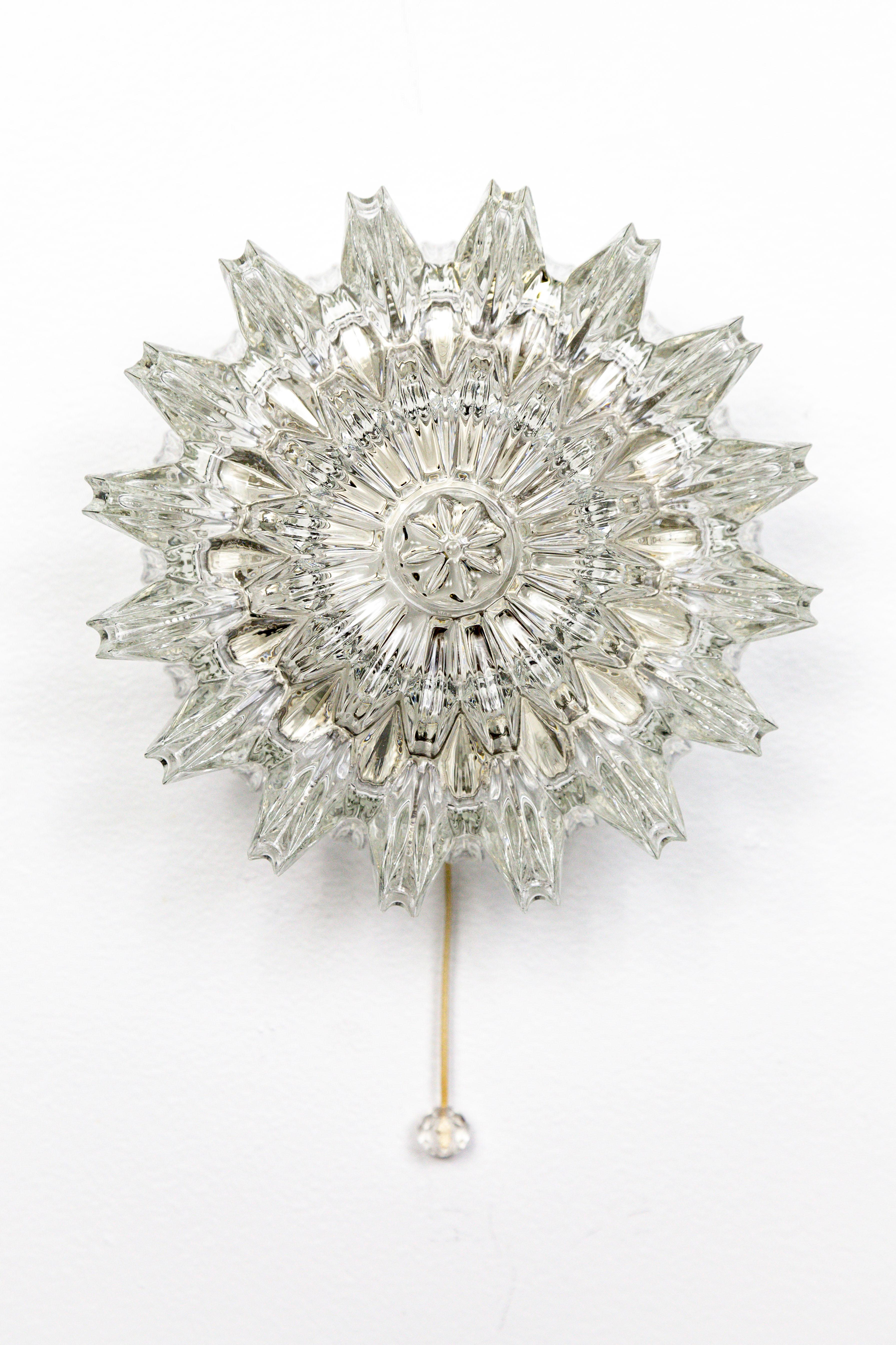 A rare style Limburg sconce; the molded glass is a beautiful, intricately detailed, sunburst shape. This petite fixture is equipped with a decorative pull chain switch and medium base, porcelain socket, and original backplate, 1960s, Germany.