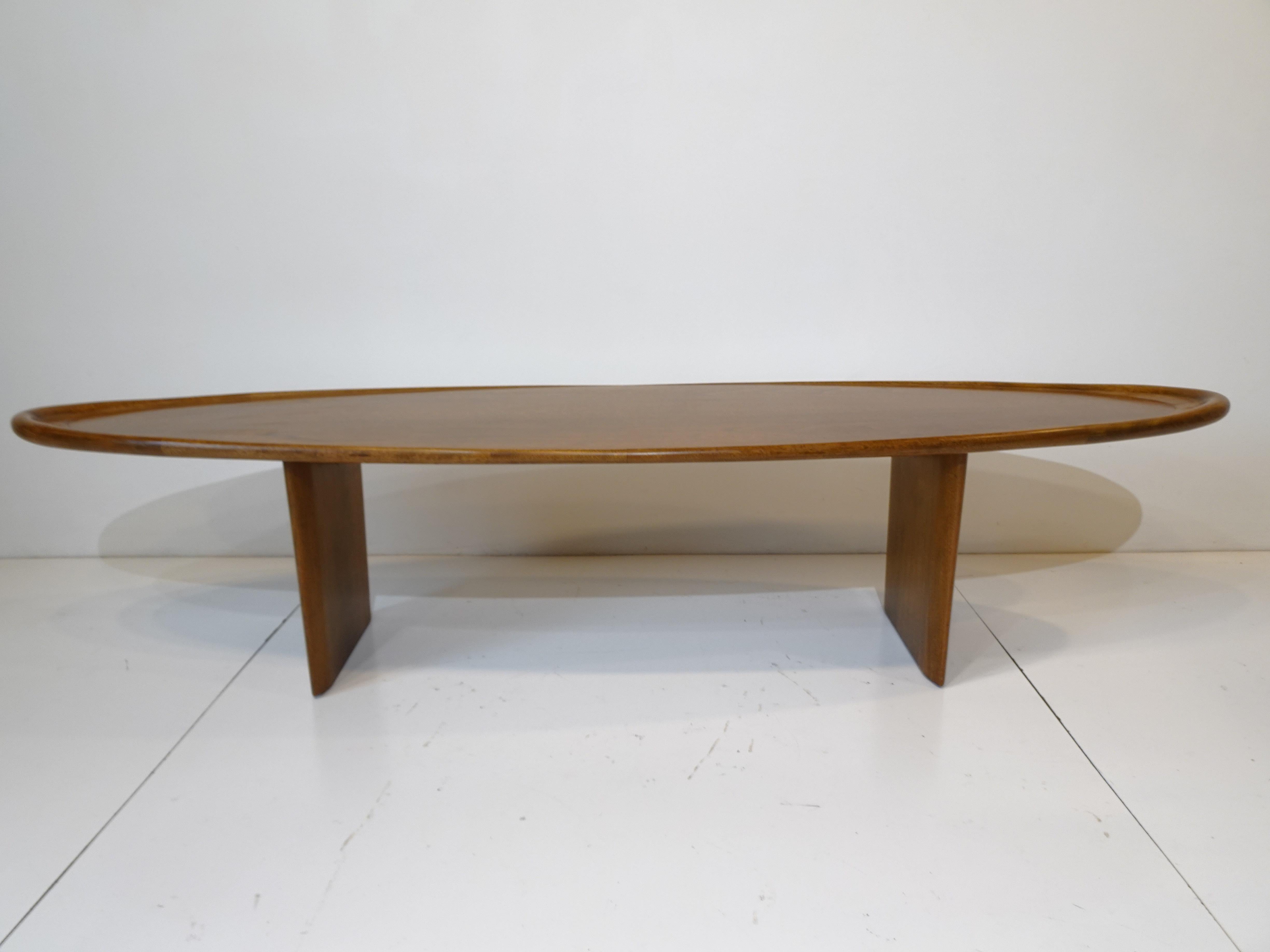 A rare elongated oval surfboard styled medium toned mahogany coffee table with rounded rolled upturned lip sitting on tapered plinth bases . The craftsmanship of this table is outstanding with great details through out and the grain of the mahogany