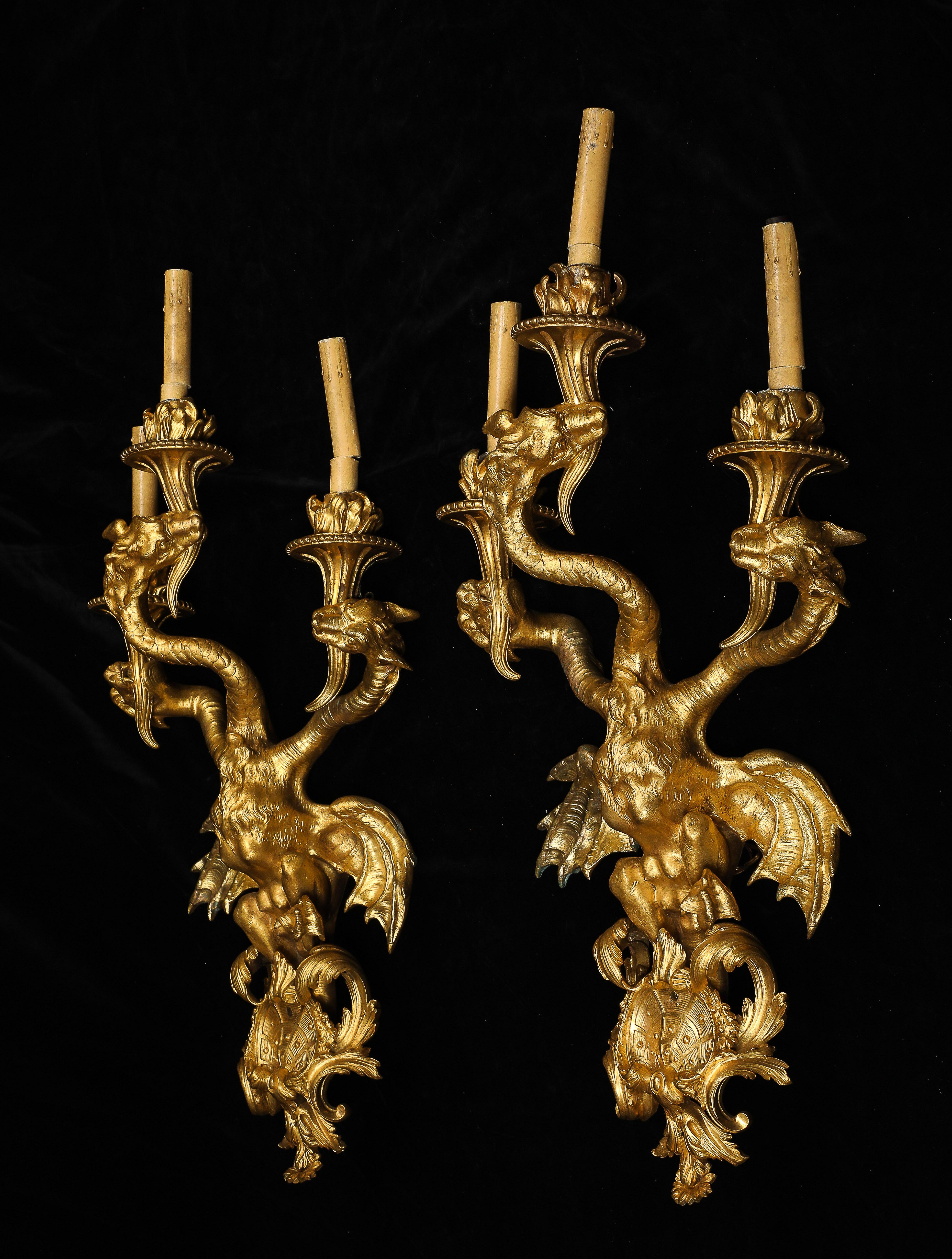 Rarissima coppia di candelabri francesi a tre bracci con testa di drago in ormolu del XIX secolo, secondo i modelli di Nicolas Pineau. Ogni candelabro è interamente fuso in ormolu e costruito con un corpo centrale sormontato da tre rami che si