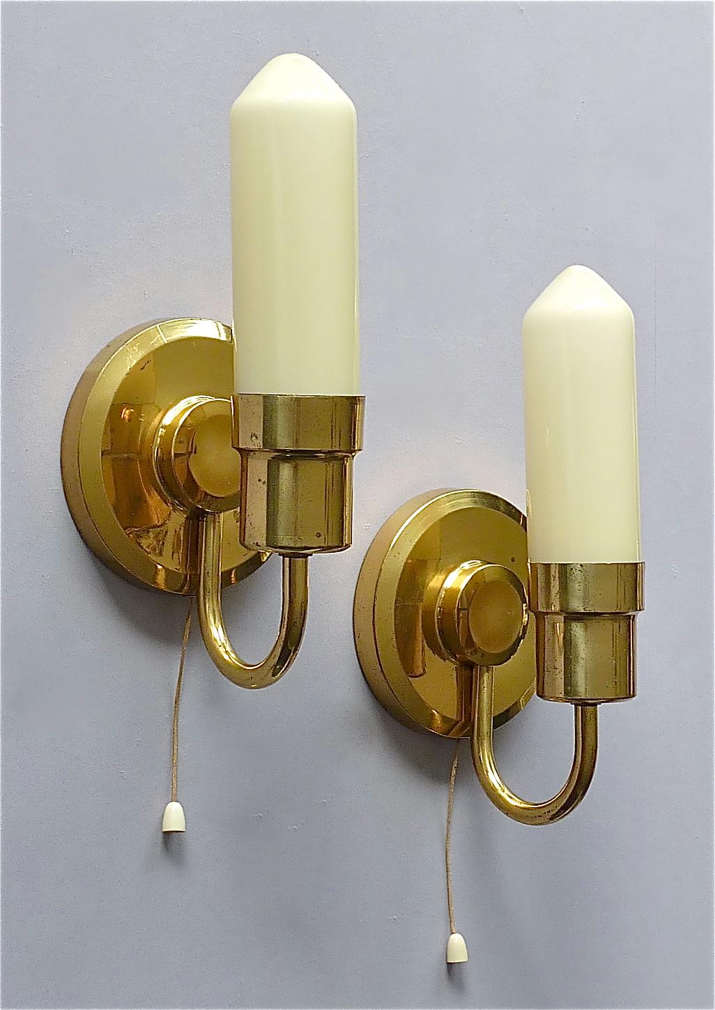 Cool and rare Austrian or Scandinavian Mid-Century Modern sconces in Paavo Tynell Taito Oy Style, circa 1950s. The wall lights which are made of patinated brass with faint yellow opaline candle glass tubes and threat-switches are 24 cm / 9.45 inches