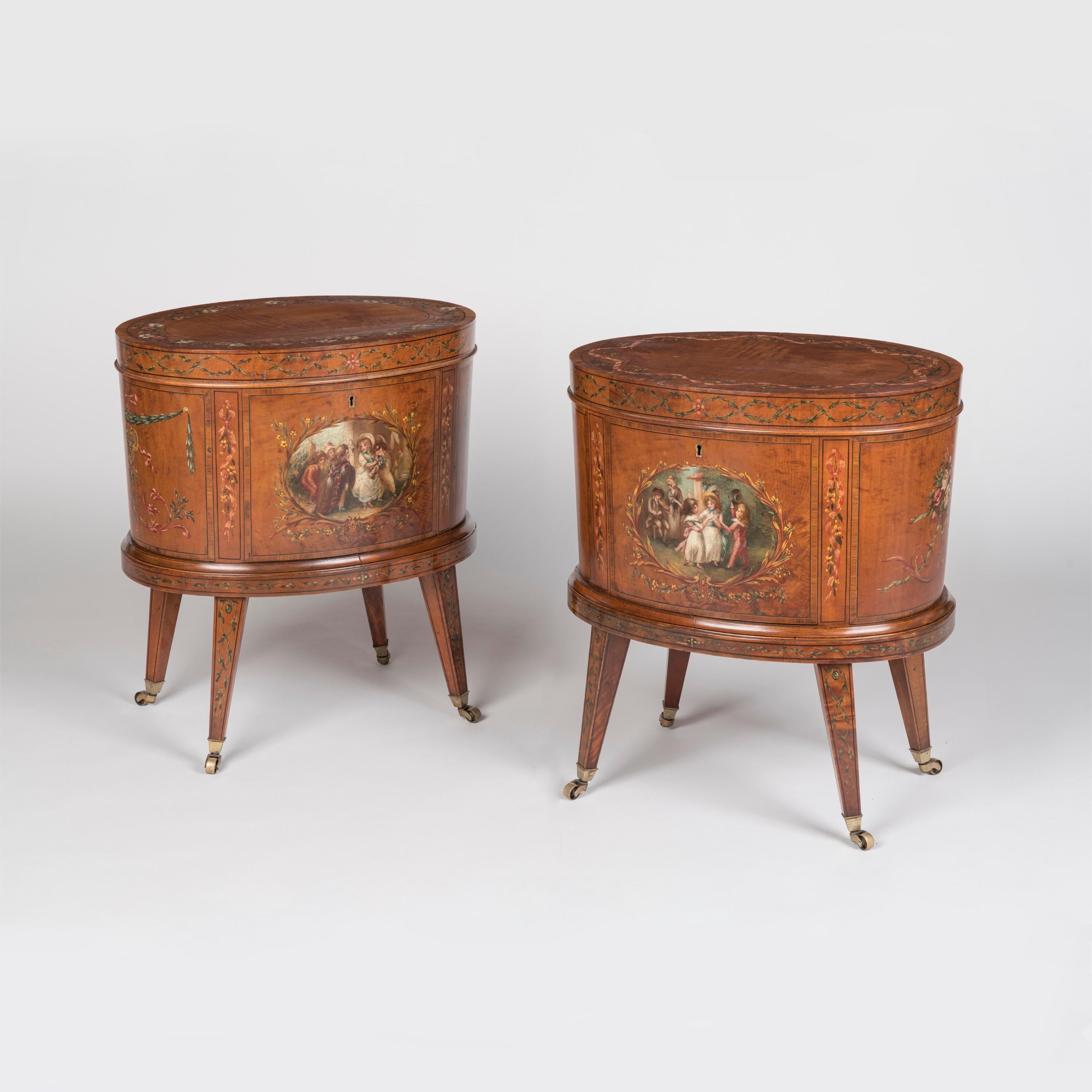 A Rare Pair of Cellarettes 
in the Adam Manner

Of elliptical form, constructed in Satinwood, hand painted with floral attributes, and 'Angelica Kauffman' style cartouches of le beau monde, in polychromes; rising from castor shod tapering and