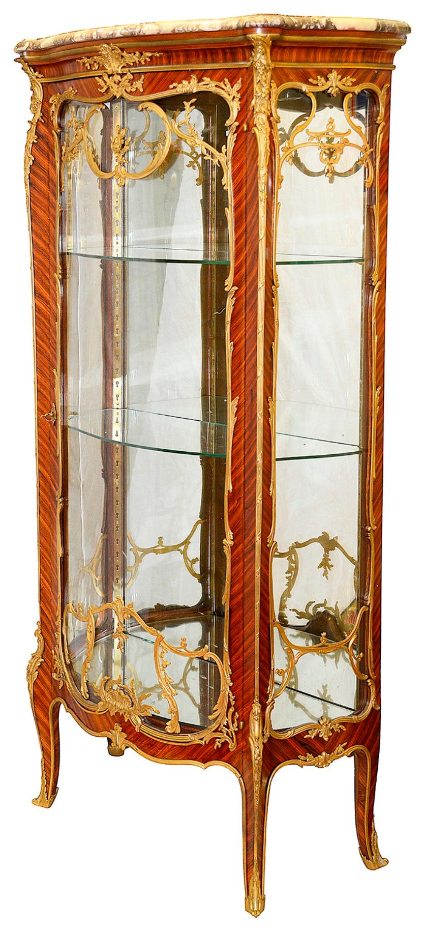 Magnifique et rare paire de vertus de style Louis XVI de la fin du XIXe siècle, chacune avec son plateau de marbre d'origine, de belles montures en bronze doré, les portes en verre à façade serpentine s'ouvrent pour révéler des étagères en verre