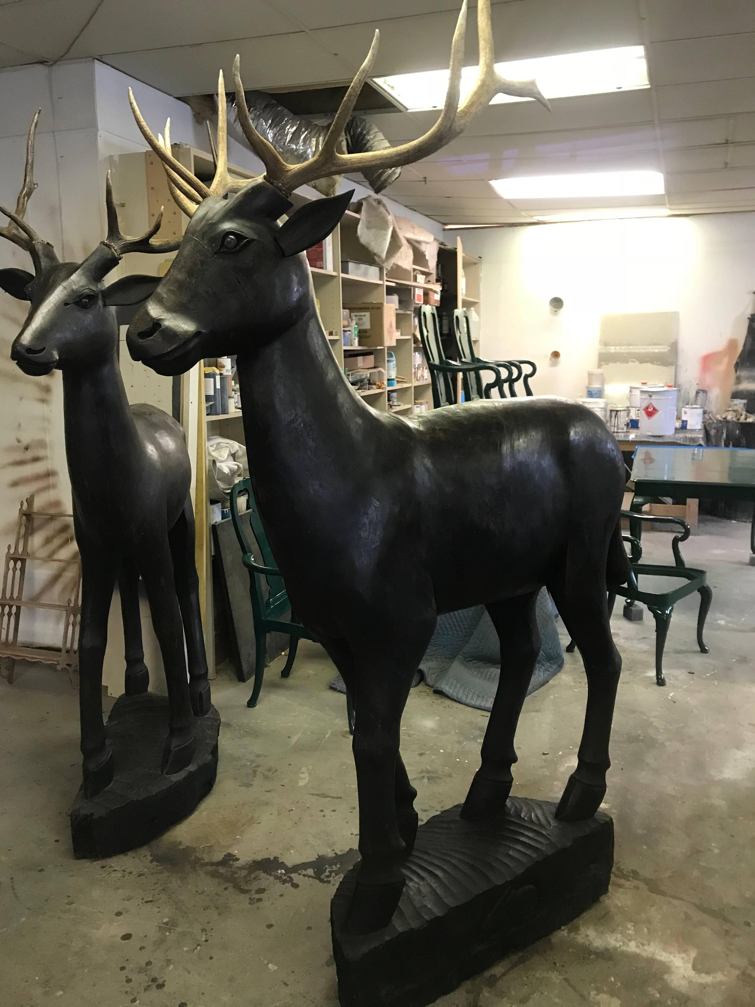 Pair of 20th century carved wooden Folk Art style deer. Appear to be carved from 1 large piece of wood. Deer are topped with removable elk antlers. Both have checks and cracks due to being exposed to weather which adds to the wonderful Primitive