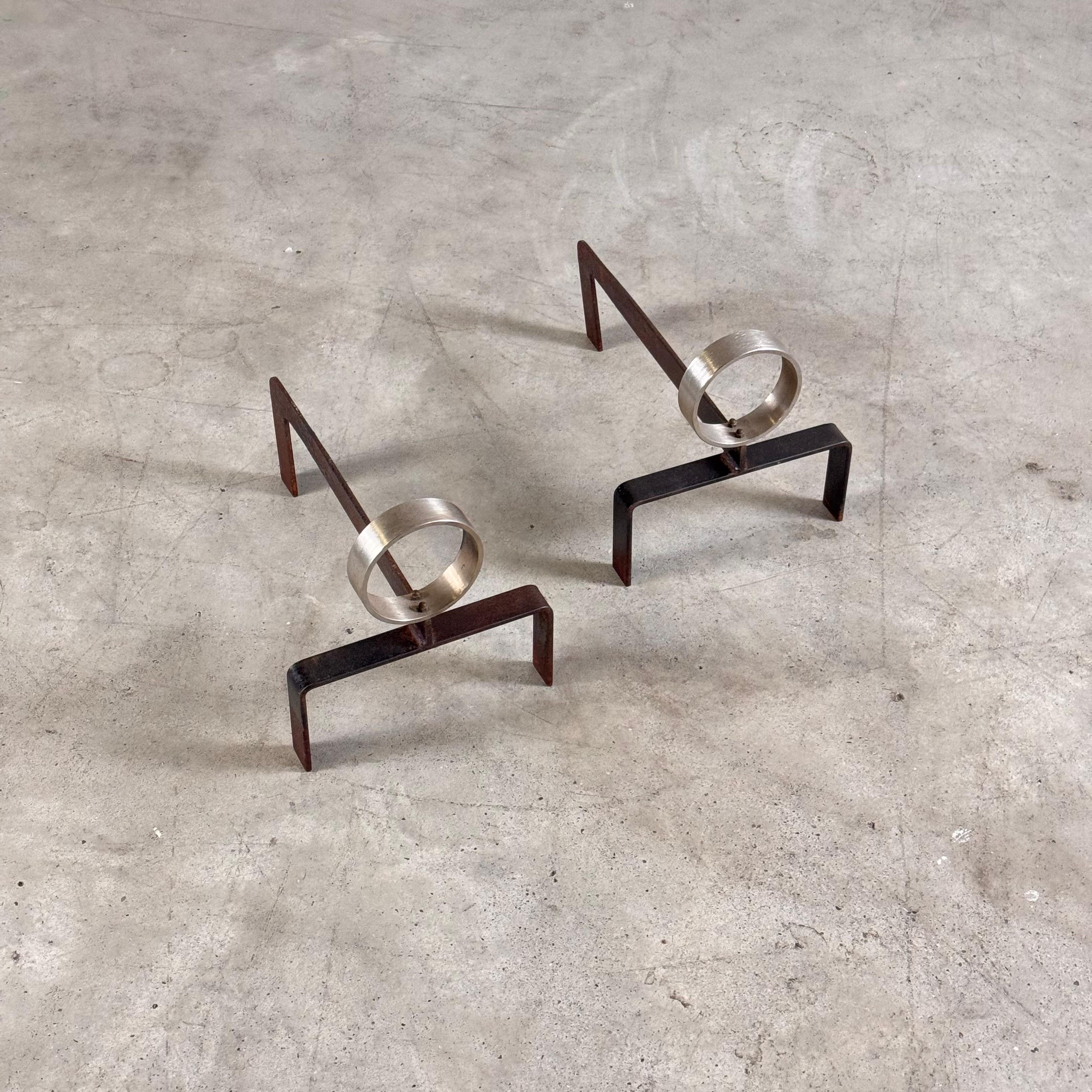 Une paire de chenets frappante et très avant-gardiste, conçue par Melchiorre Bega en 1960. Réalisées dans une combinaison audacieuse d'aluminium et de fer, ces pièces se distinguent par leur design sculptural, où un élément circulaire en aluminium