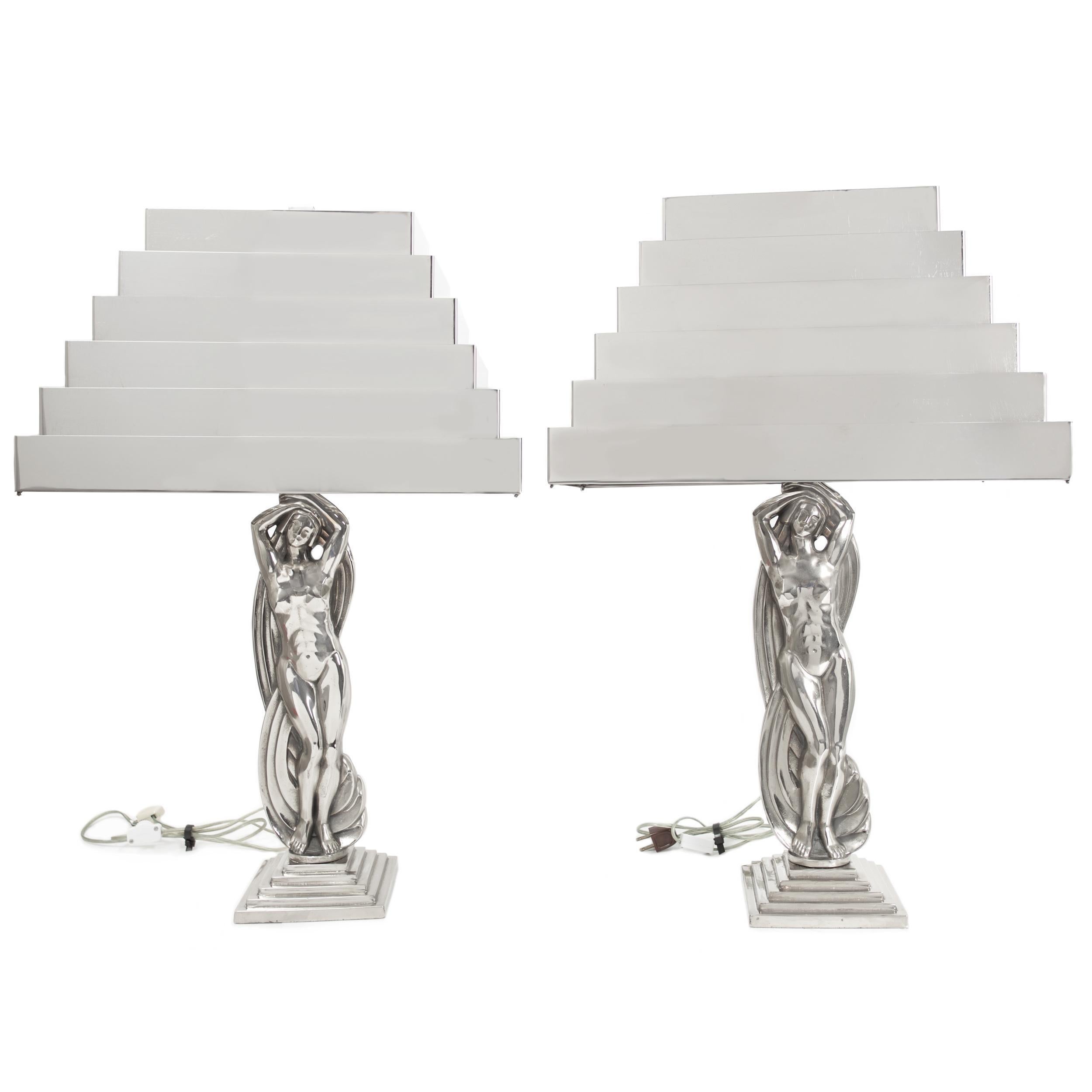 A remarkable pair of Art Deco period lamps depicting stylized female figures standing before swirling twists of fabric over a stepped base raising the lighted elements behind a chromed steel stepped shade. This is a collapsing form designed with