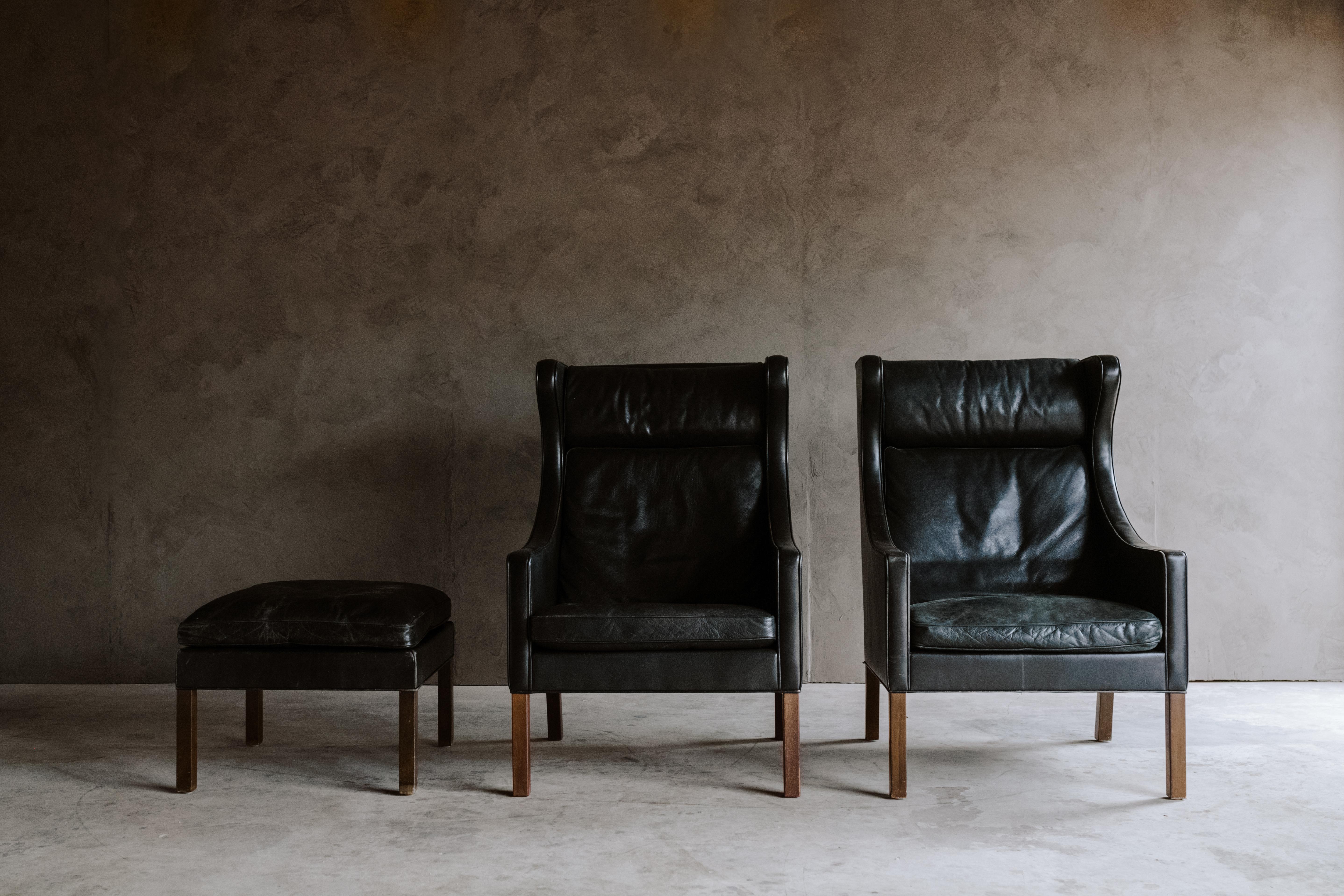 Rare Pair of Børge Mogensen Wingback Chairs, Denmark, 1970s. Original black leather upholstery with solid teak legs. 

One ottoman included. Measures: H 18, W 22, D 22.
