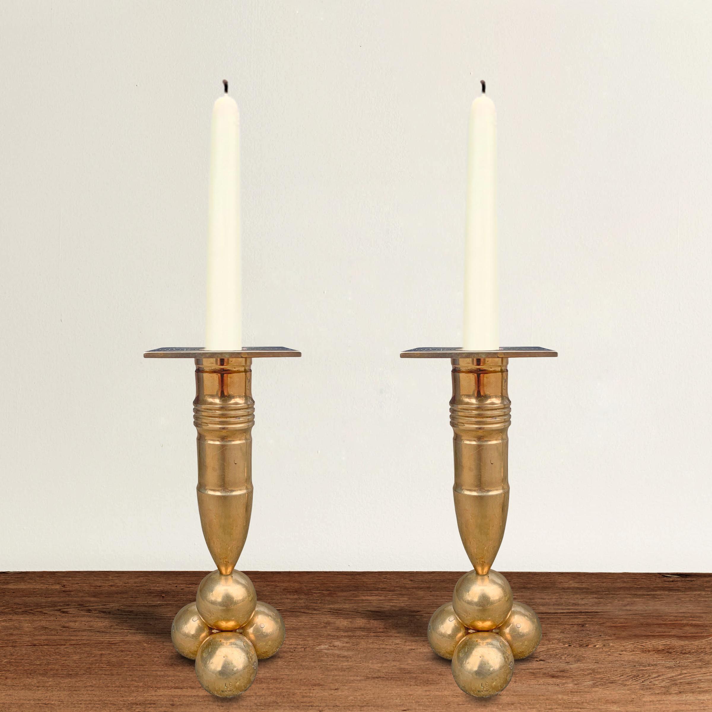 A rare pair of mid-20th century bronze candlesticks with artillery shell stems, each resting on a stack of cannonballs, by Swedish designer Gusum Mässing.