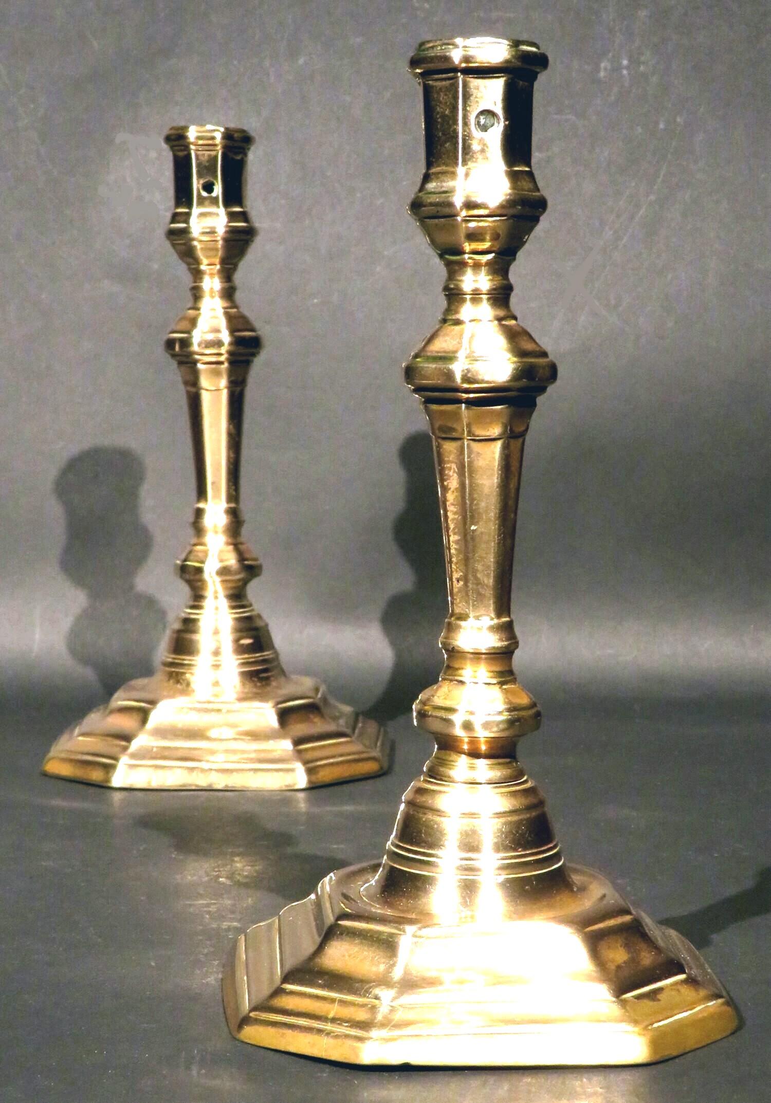 A very handsome and rare pair of early 18th century bell metal candlesticks, both showing flaring stems with cushioned & faceted knops terminating to octagonal panelled nozzles, rising from welled and stepped octagonal bases. Both exhibiting an