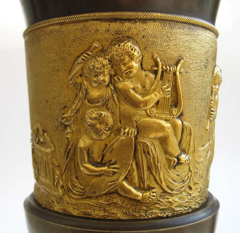 A rare and decorative pair of early 19th century Empire gilt and patinated bronze vases of campana form on a stepped square marble base. The everted egg-and-dart rim above a finely chased frieze depicting putti playing music.

This or a similar