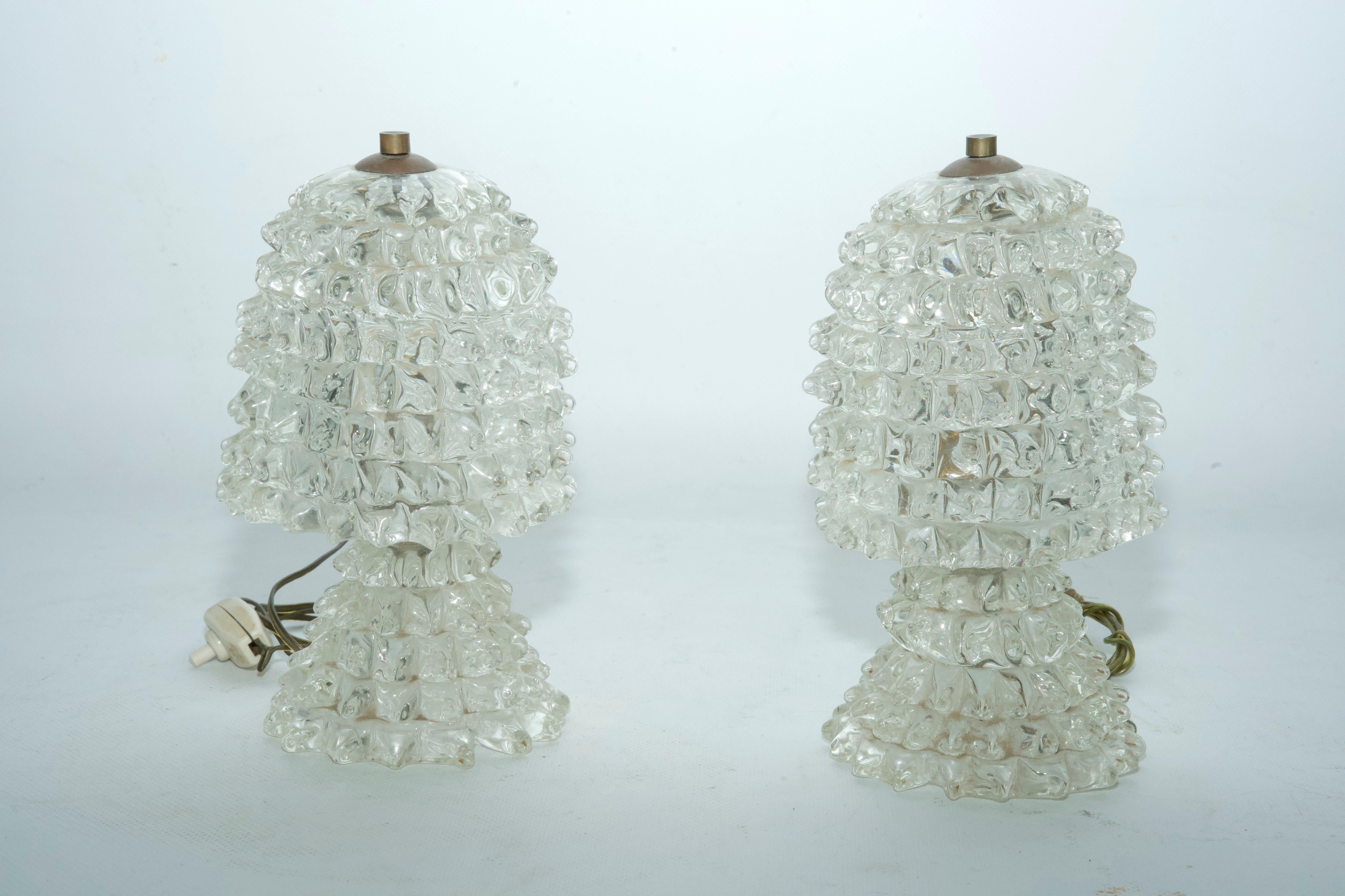 This rare pair of table lamps, crafted by Ercole Barovier in Italy during the 1940s, showcases the renowned “Rostrato” technique, a hallmark of Murano glass artistry. The surface of each lamp is adorned with meticulously hand-applied glass spikes,