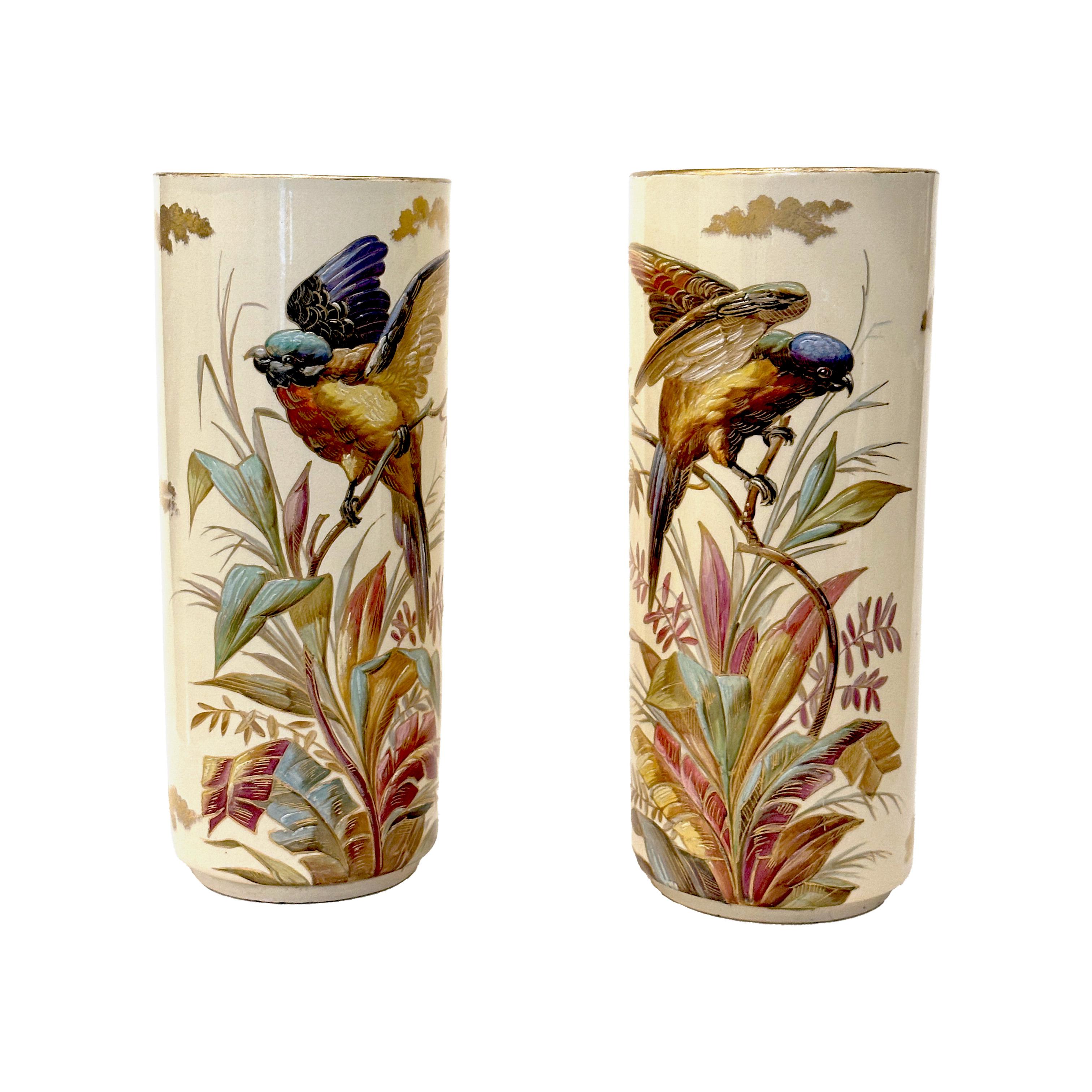 An elegant pair of cylindrical sleeve-form vases in fine cream-glazed faience, exquisitely hand-painted with vibrant exotic birds perched amid lush foliage. The detailed polychrome decoration is masterfully rendered, with rich tones and precise