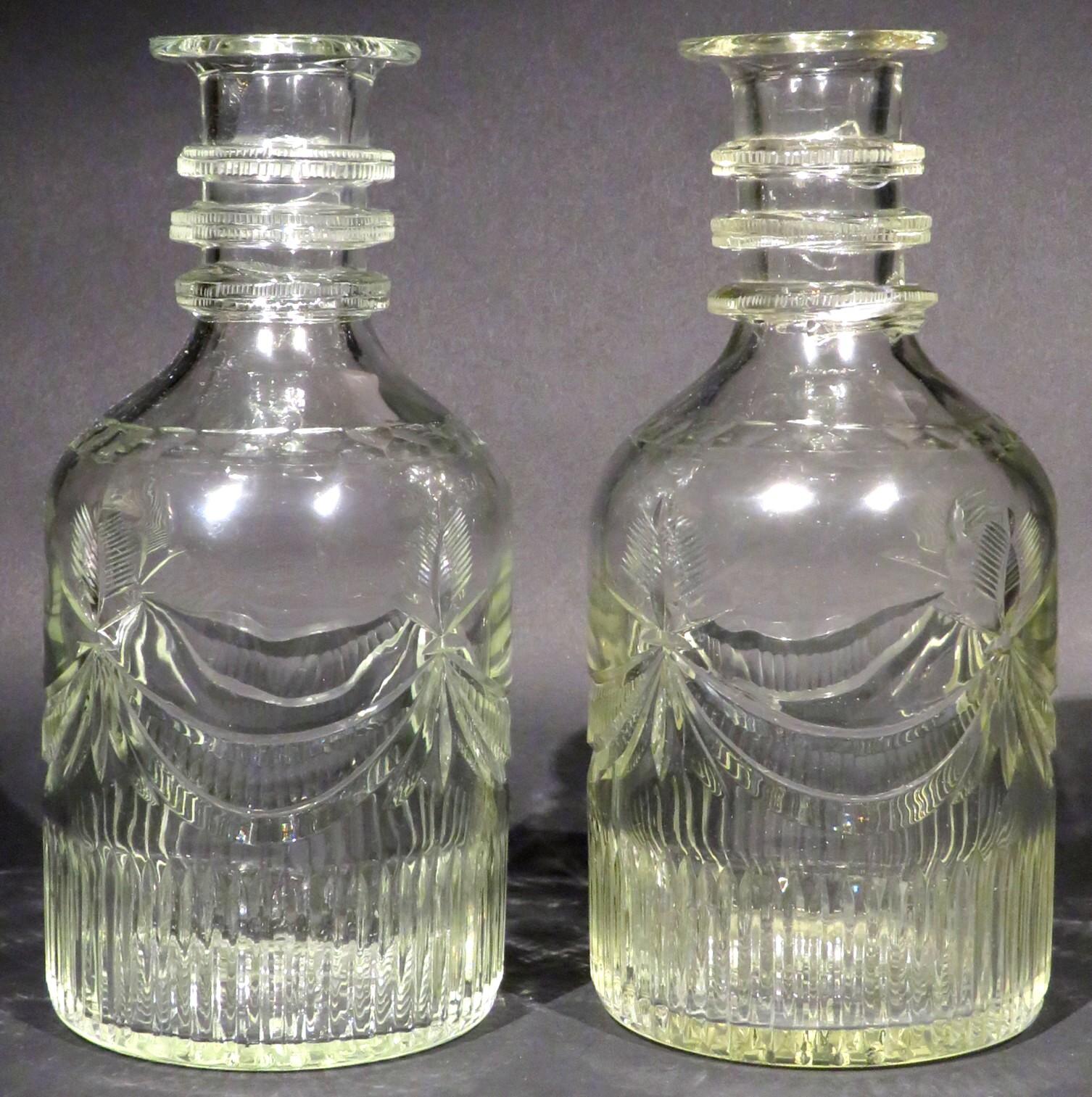 An extremely rare & robust pair of Irish Georgian Cork Glass Company wine carafes. 
Both of mallet form decorated with basal cut flutes & engraved swags rising to feathered triple ring necks. 
The undersides of their bases bearing moulded factory
