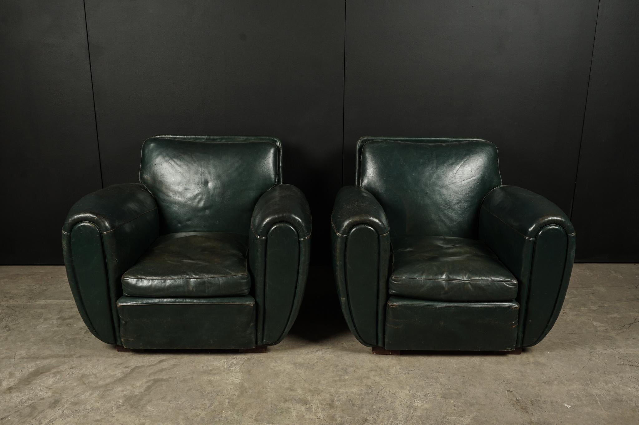 Rare pair of leather club chairs from France, circa 1950. Original green leather upholstery with studded nail heads on back. Early deco model with large curved arms.