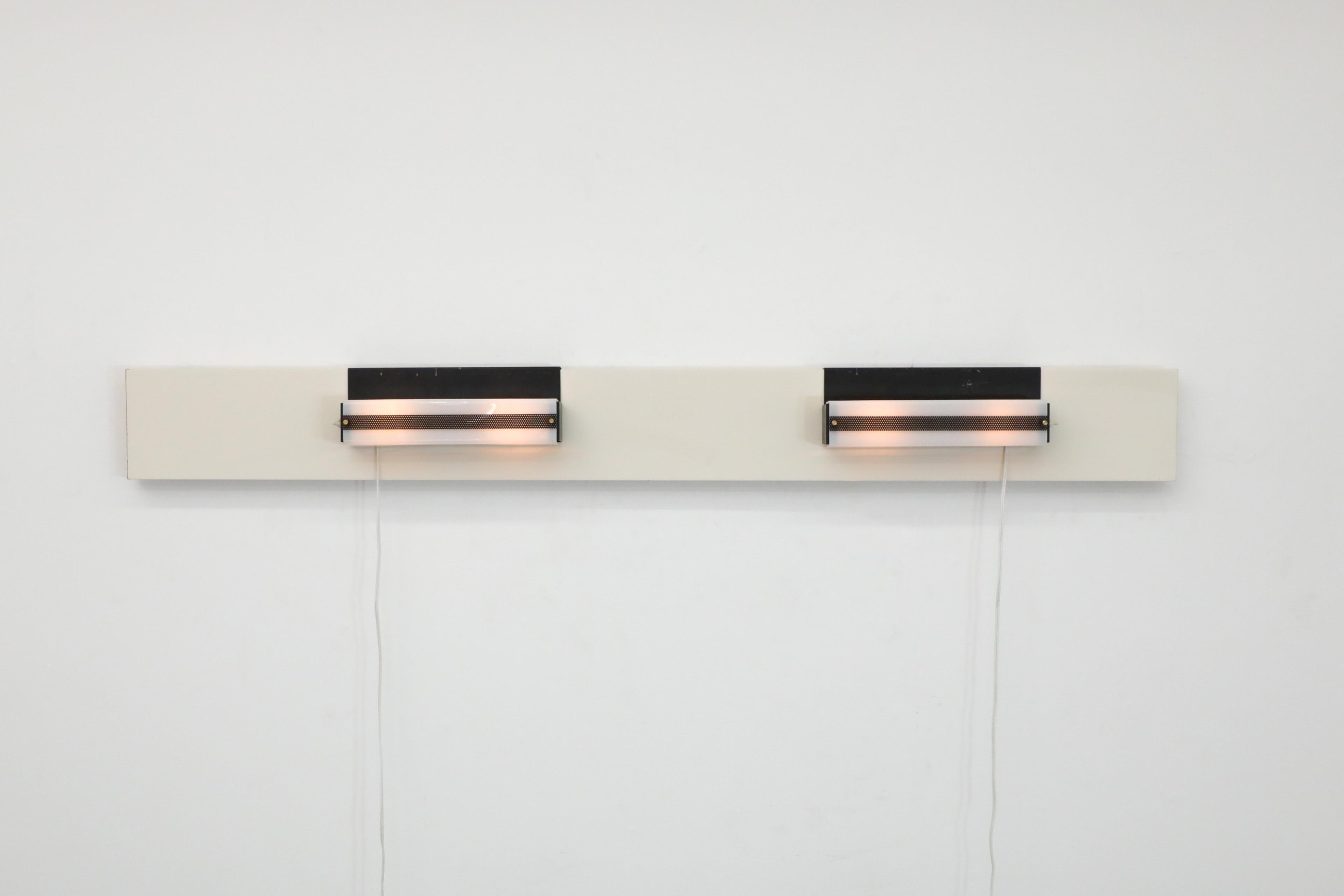 Coppia di luci rettangolari con corpo in metallo smaltato nero, paralumi in plexi bianco e accenti in ottone nero perforato. La staffa posteriore delle luci si aggancia a superfici spesse fino a 2