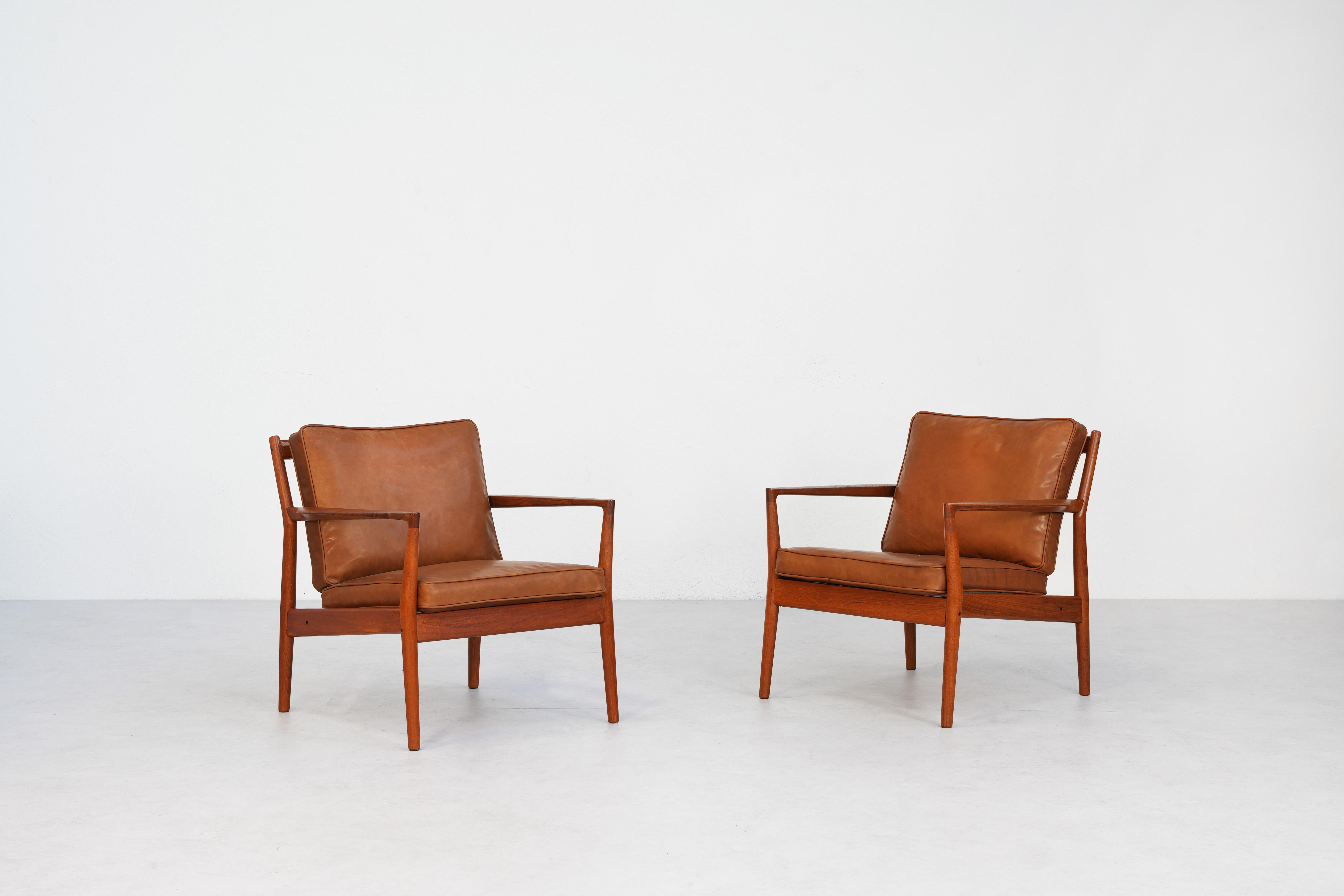 A pair of incredibly rare teakwood lounge chairs produced by Børge Jensen in Denmark in the 1960s. The frames feature sculptural blade arms and angled back slats. The feather cushions have been covered in new cognac brown aniline leather. Both
