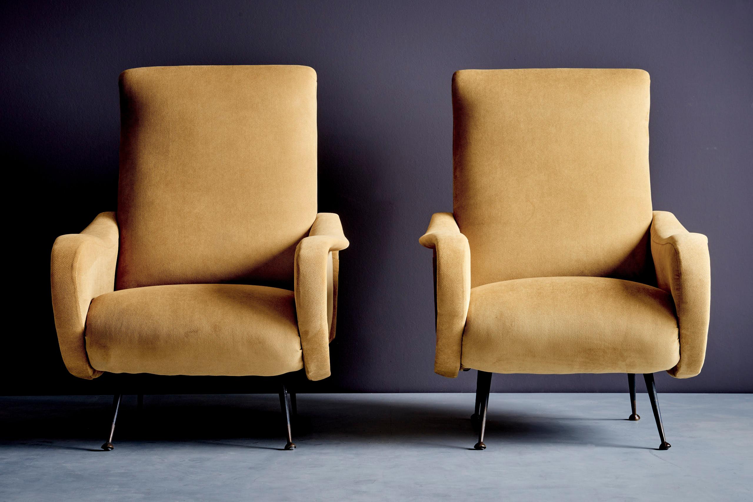 This pair of Italian lounge chairs from the 1950s is designed in the manner of Gastone Rinaldi, featuring a striking sculptural form. These curved armrests and comfortable seats are resting on sleek black metal legs. These chairs embody Rinaldi's