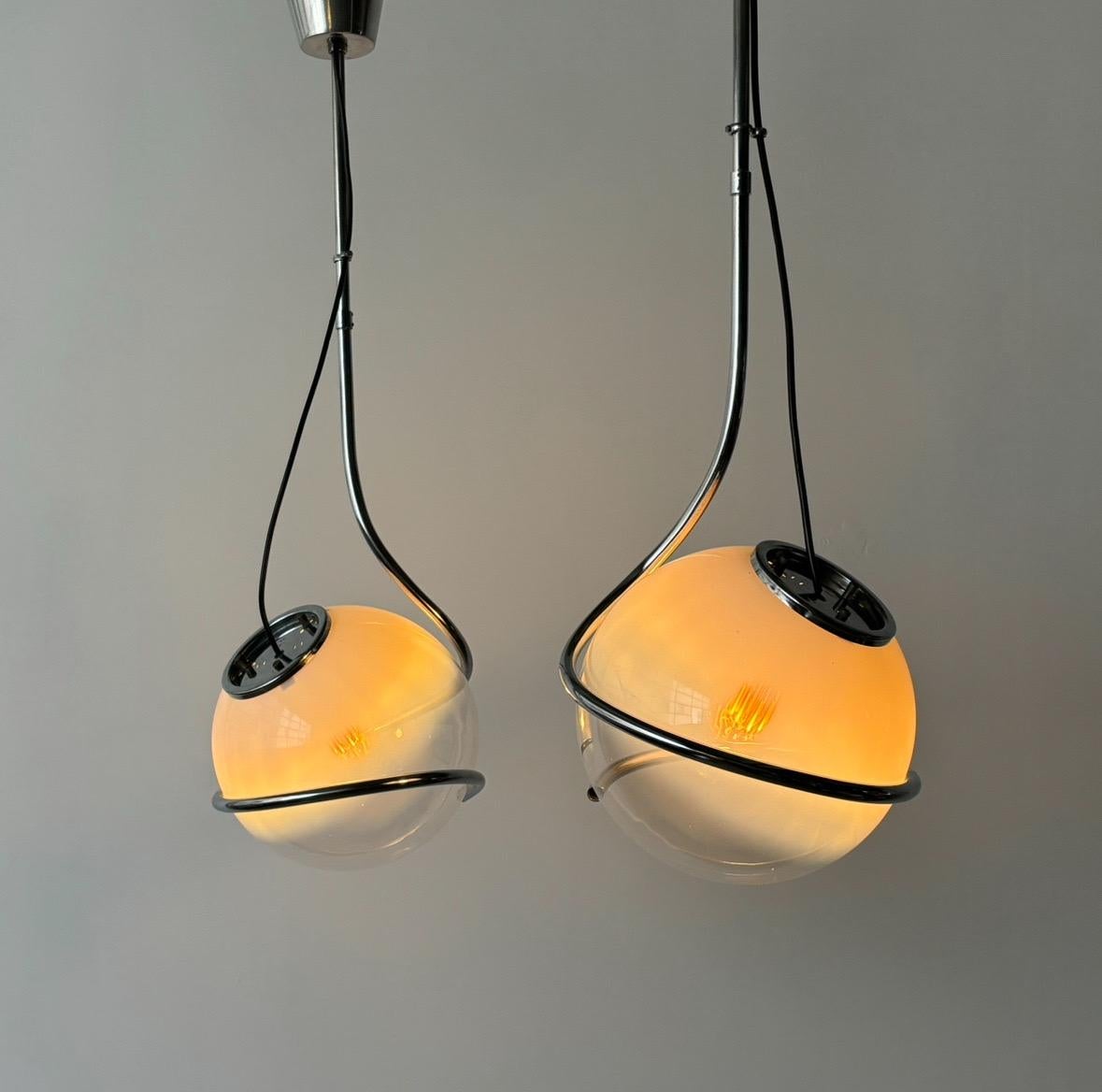 An Italian-made Space Age Pendant from the 1960s to 1970s features a Murano glass sphere transitioning from teal to transparent. It is elegantly held and supported by a chrome metal tube, reminiscent of a Cobra snake's grip.
•

Born in Rome in 1935