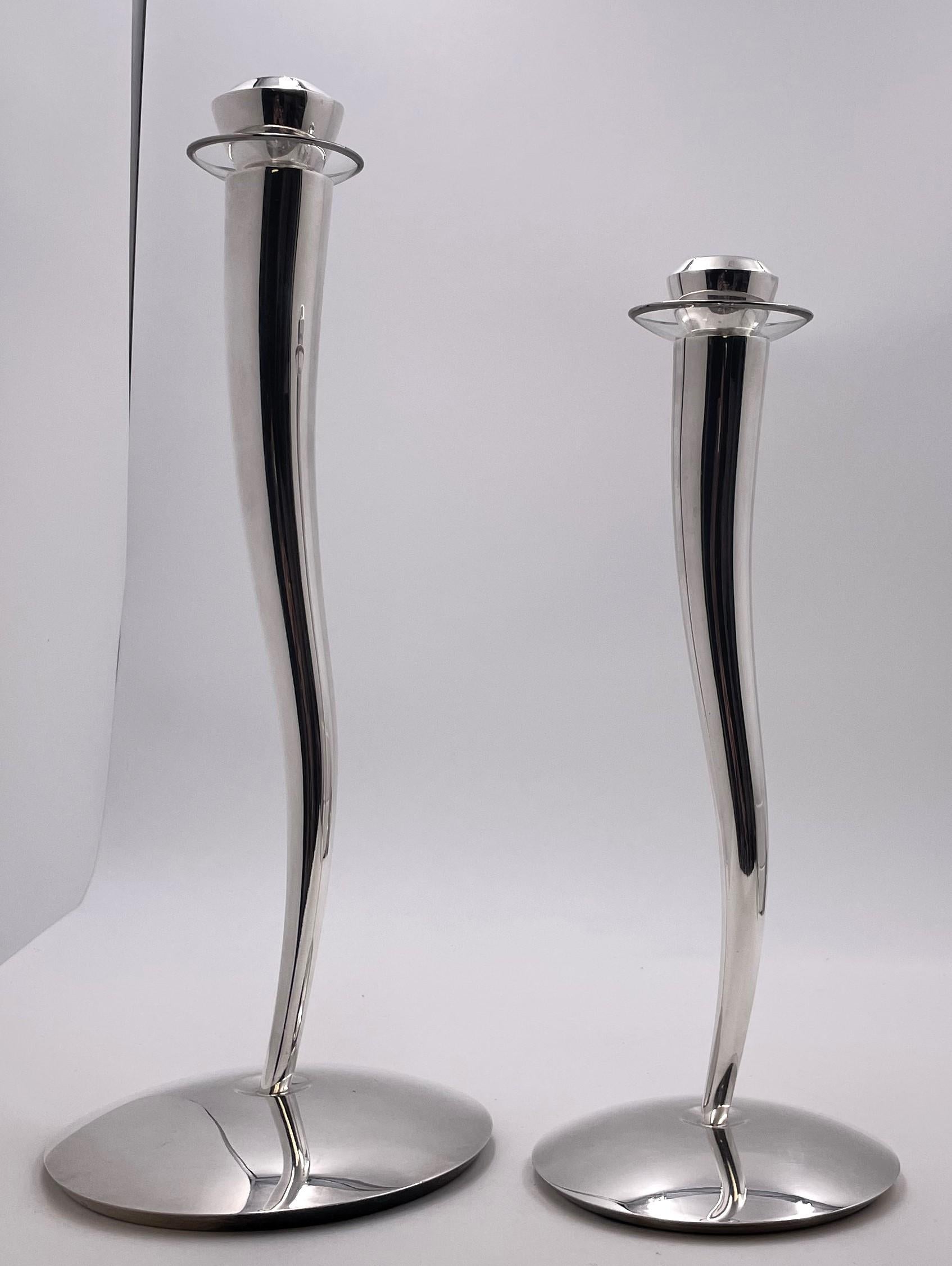 Rare pair of Pomellato sterling silver candlesticks, accompanied with glass bobeches, in Mid-Century Modern style with an elegant, geometric design. The tallest measures 16'' in height by 7'' in diameter at the base while the other measures 13'' in