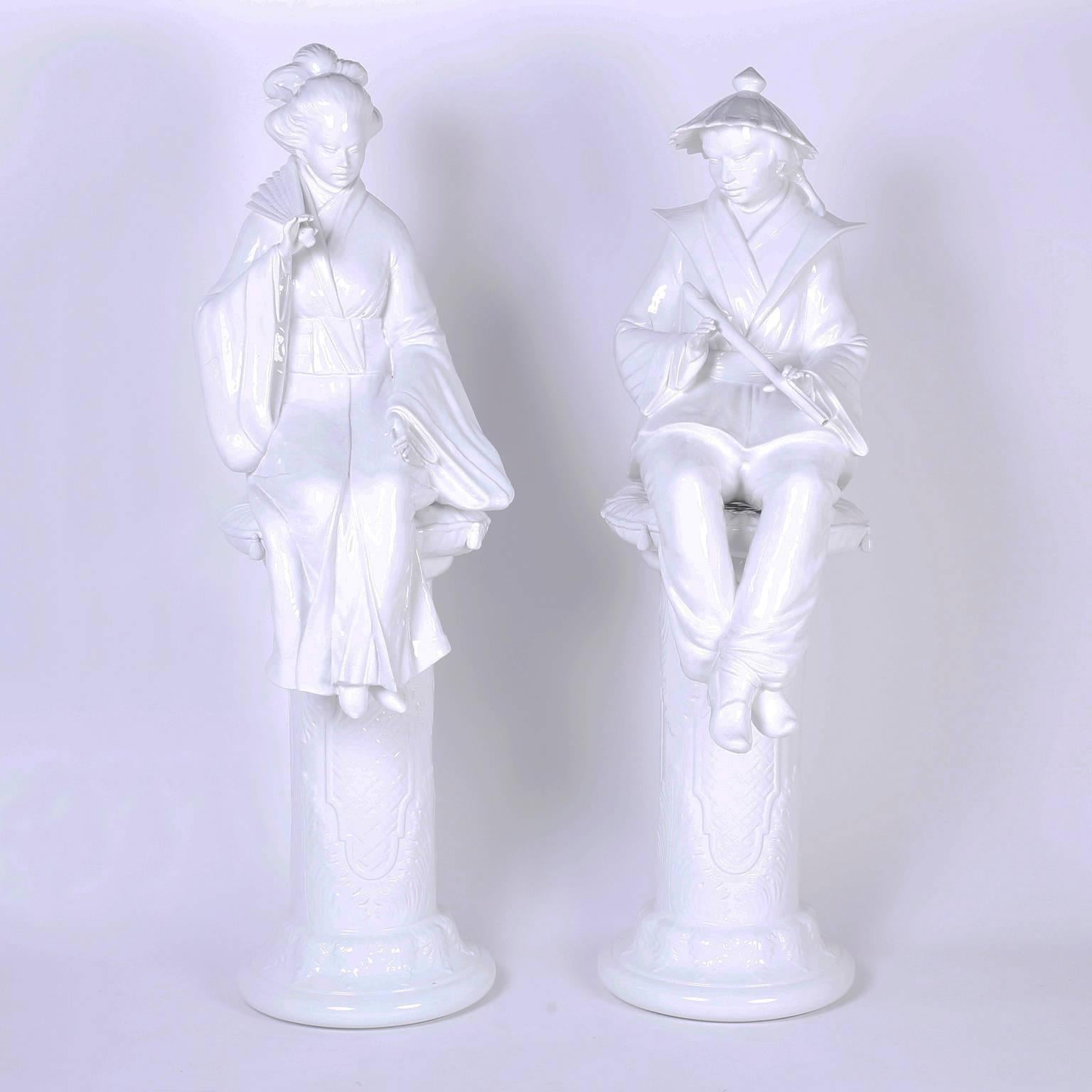 Chic pair of porcelain figures crafted in three pieces: pedestal, pillow, and classic male and female chinoiserie figures, he with a flute and she with a fan, together an alluring, highly decorative couple for the ages. 

The male figure is 53