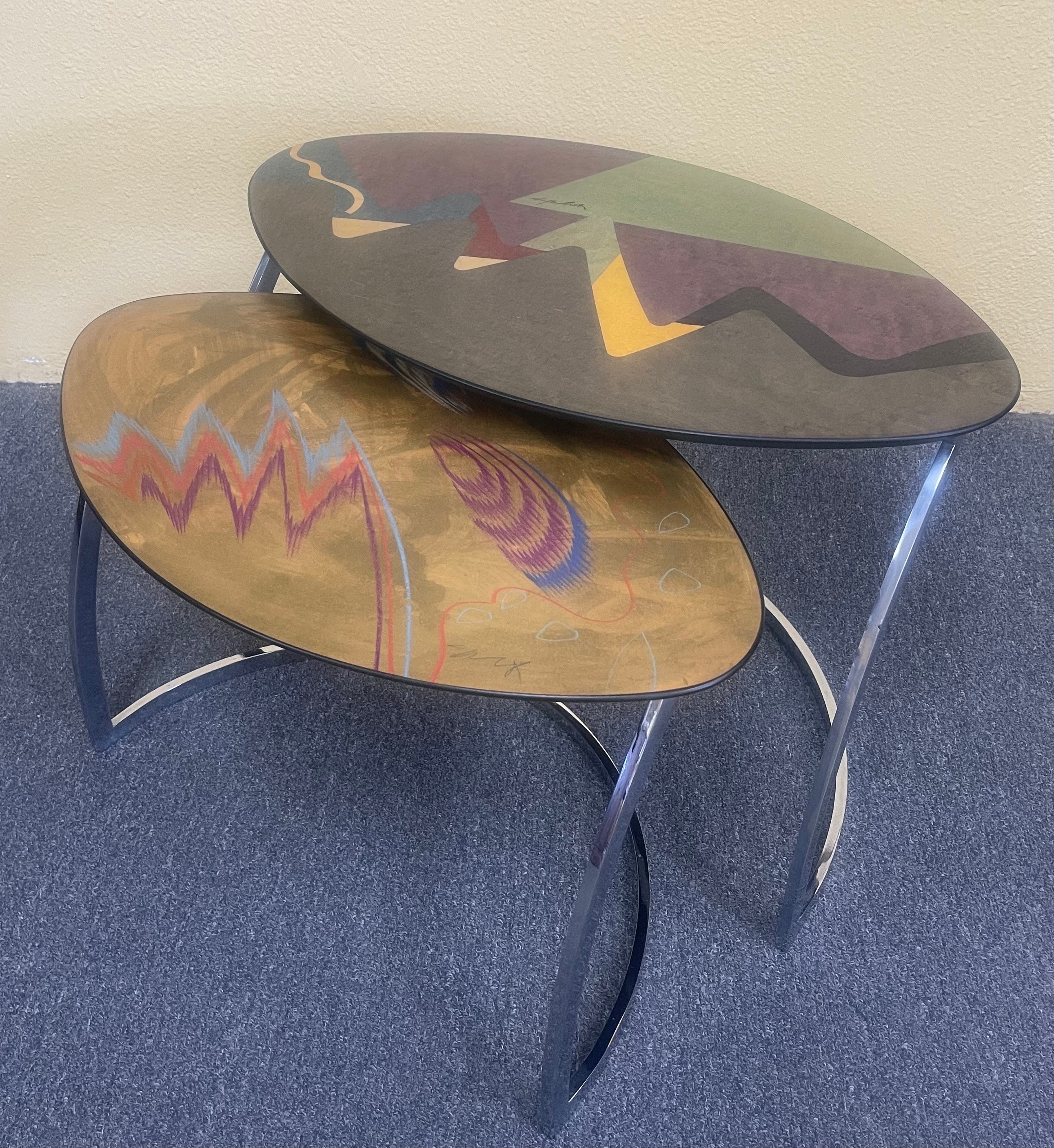 Stunning pair of Italian post-modern lacquered nesting tables signed by Pietro Costantini, circa 1990s. The table tops are made of hardwood veneer with a clear high gloss lacquer finish over acrylic painted table top designs (up close, you can see