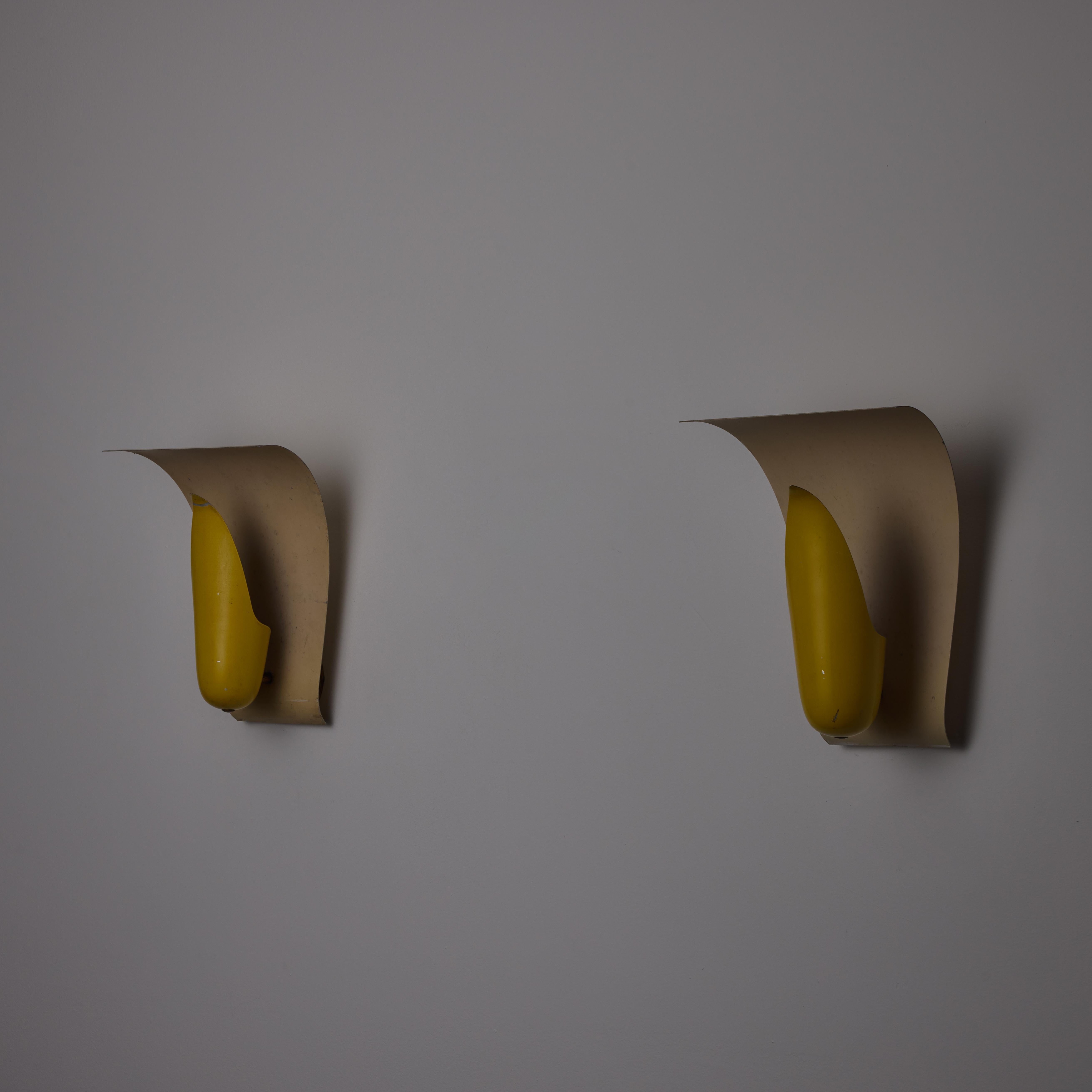 Raro par de apliques de Angelo Lelii para Arredoluce. Diseñado y fabricado en Italia, hacia la década de 1950. Una delicada y femenina pantalla amarilla esmaltada, respaldada por un reflector curvo esmaltado. La pantalla engloba un único tipo de