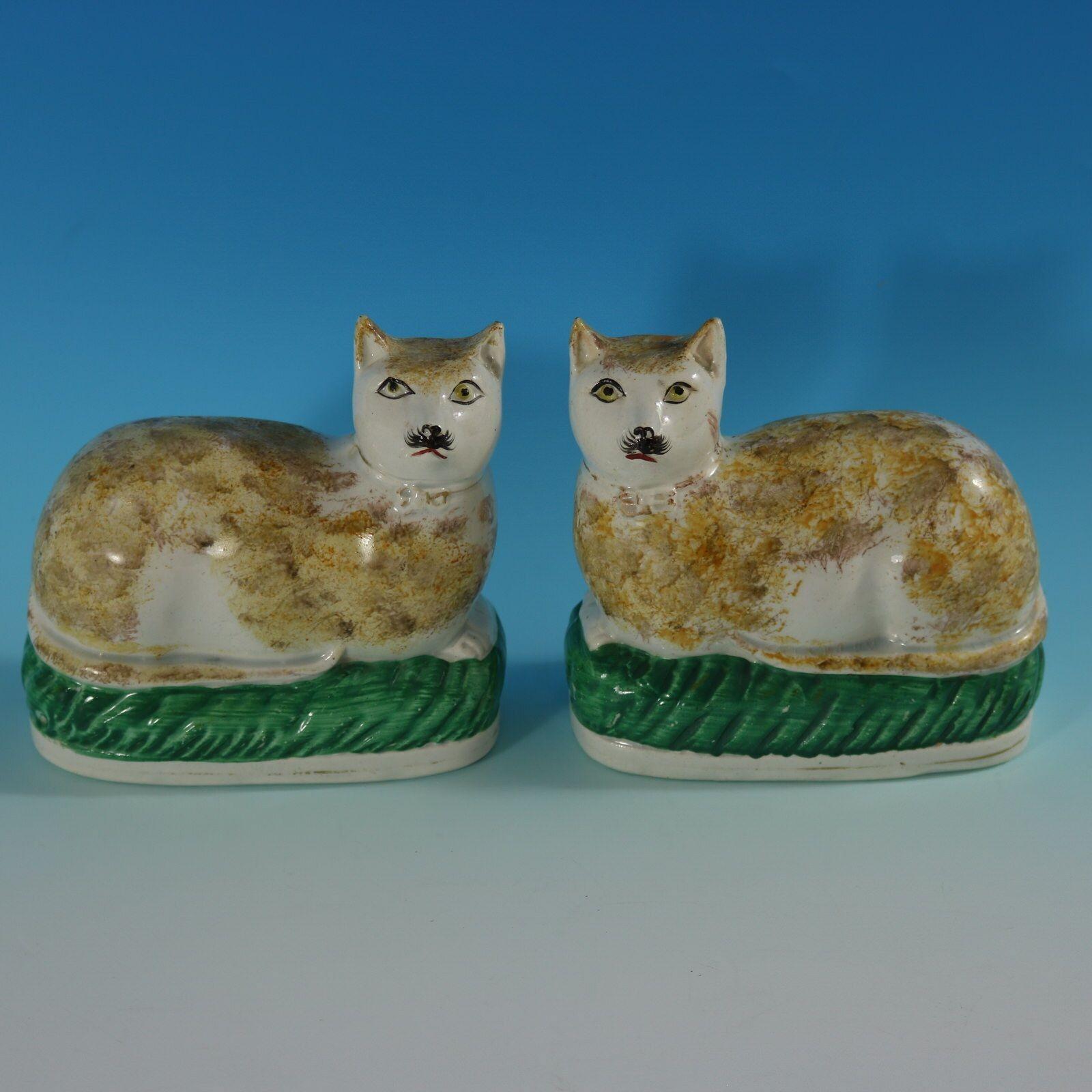 Pair of Staffordshire Pottery figures which feature a cat on a cushion, recumbent on an oval base. Dull gilt base line and embellishment.