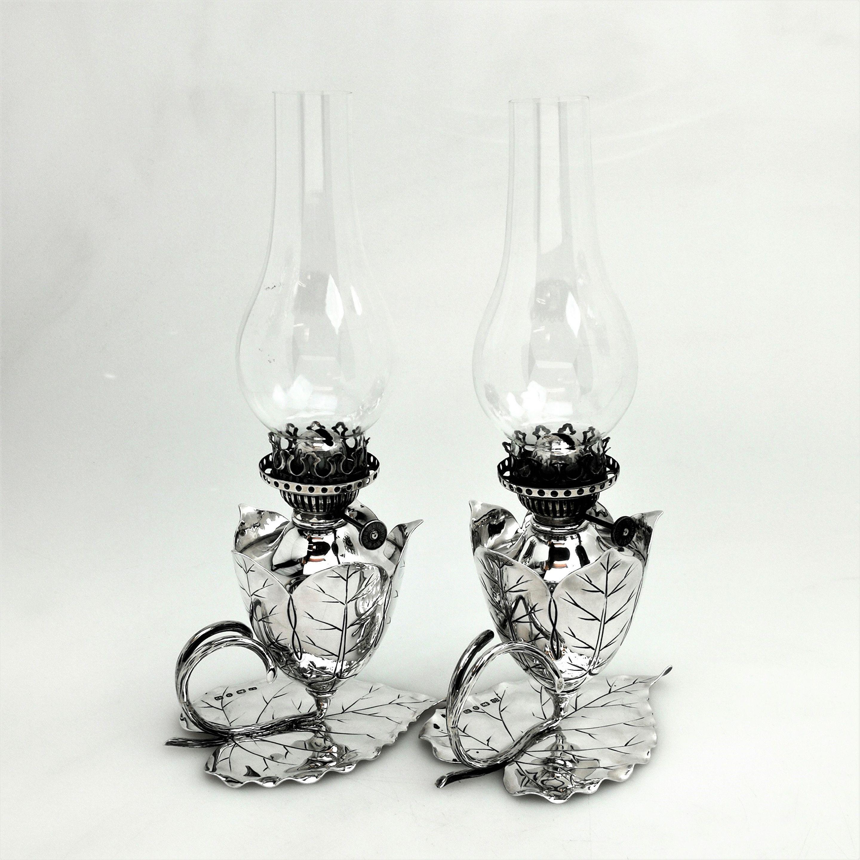 A magnificent pair of Antique Victorian solid Silver Oil Lamps with silver bases and clear glass push fit storm shades. The bases of the silver lamps are unusually shaped with a wide leaf foot and the body of the lamps made is of an open flower with