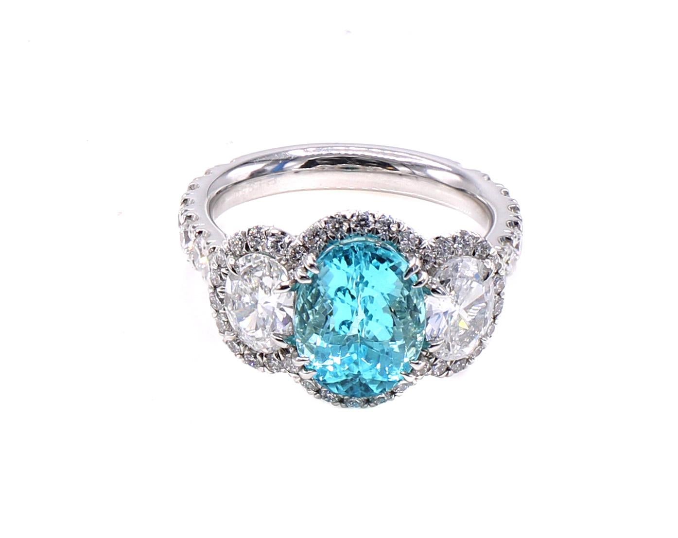 A vibrant neon blue Paraiba Tourmaline weighing 3.01 carats is the center piece of this gorgeous beautifully designed and masterfully hand crafted platinum diamond ring. The perfectly cut oval has a traditional brilliant cut on the top of the