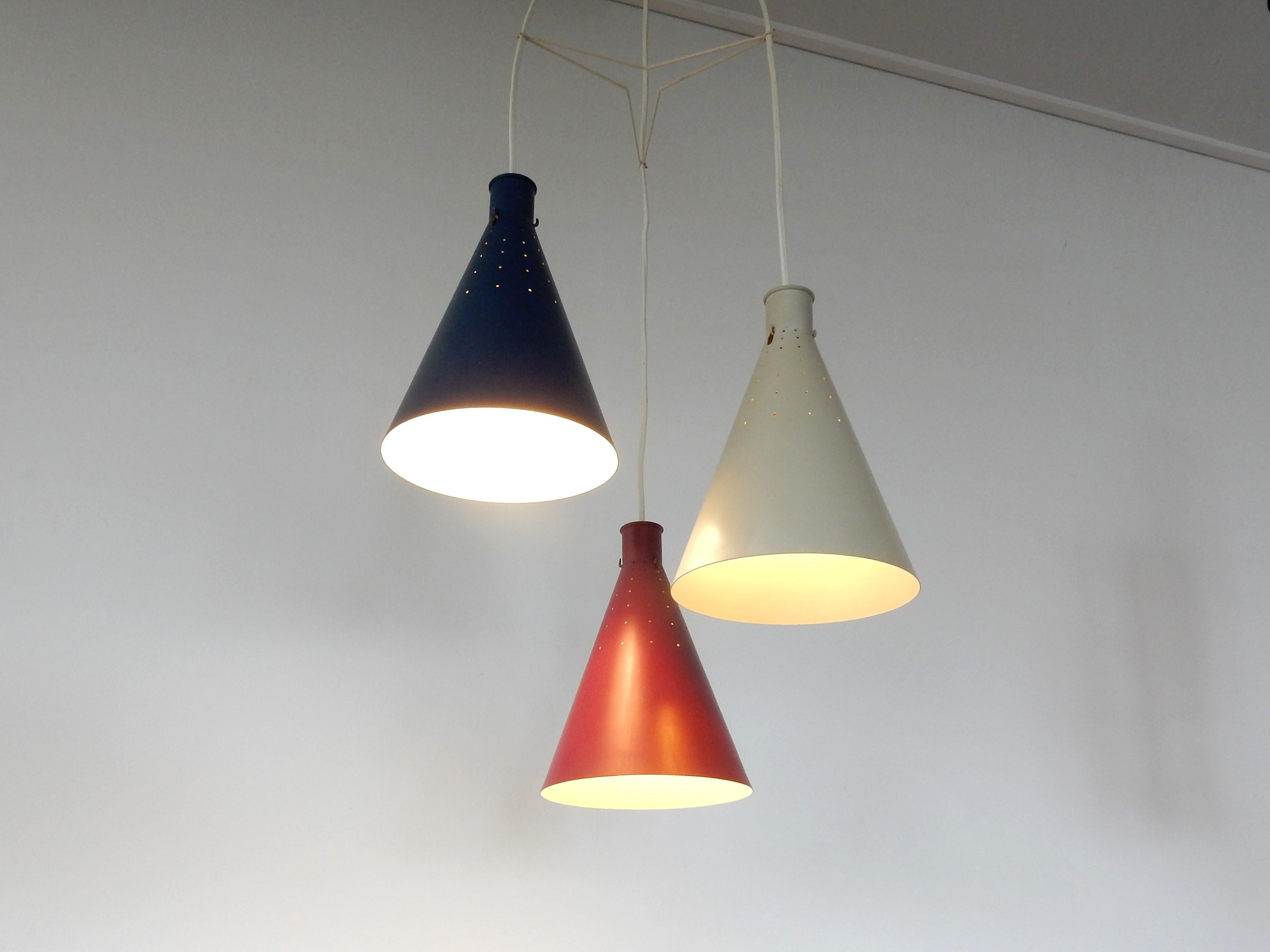This very good looking set of 3 conical pendant lamps was designed by Alf Svensson for Bergboms in Sweden in the 1950s. It consists of 3 metal shades in red, grey and blue lacquer. The shades are perforated with small holes that gives a stunning