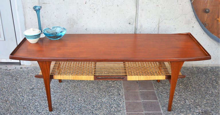 This rare and Killer Danish modern teak coffee table was designed by Peter Lovig Nielsen in the 1950s. Featuring unique flared ends, sword blade legs and a very handsome and unusually woven sculptural lower shelf. In beautiful, restored condition