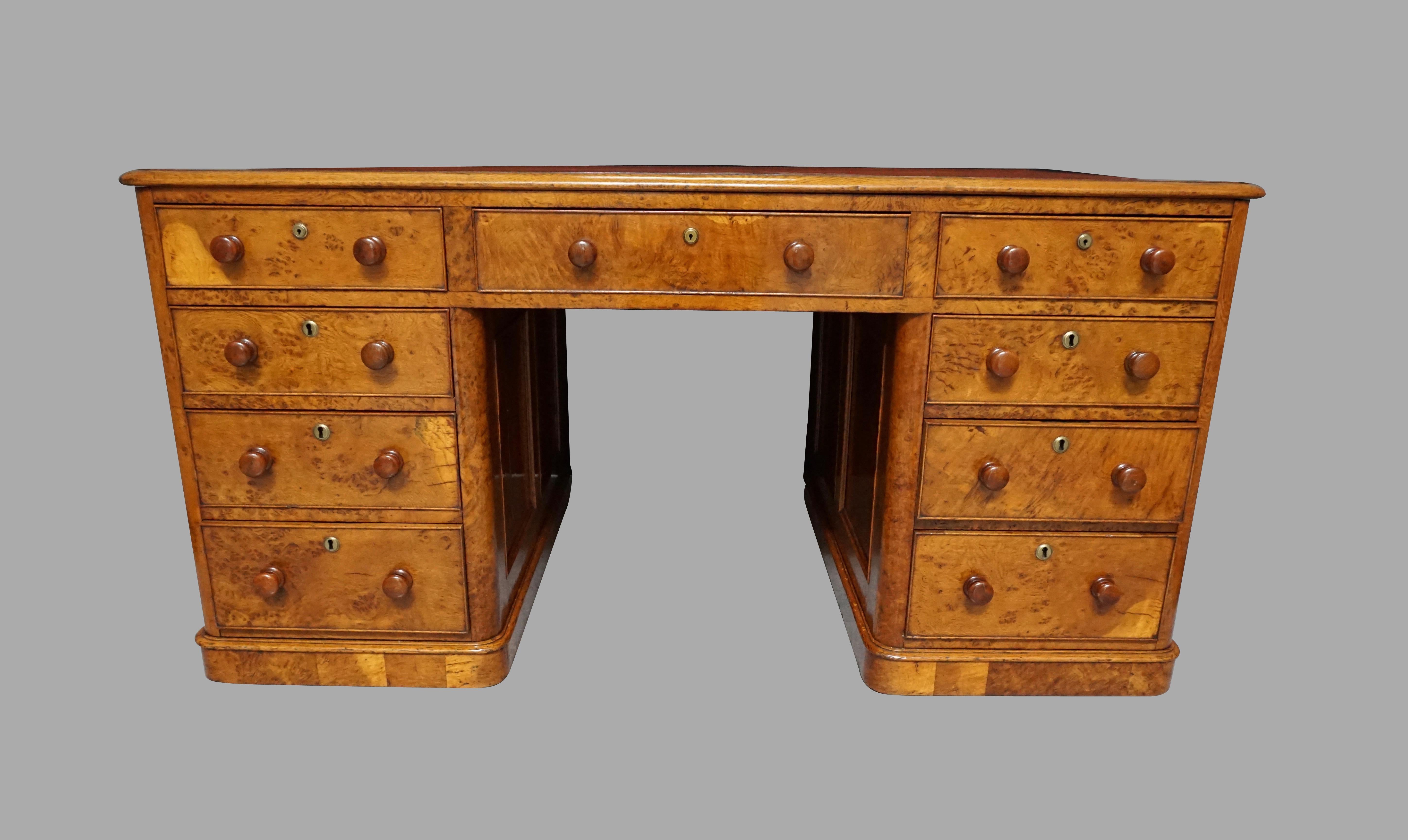 A fine quality one-piece English oak and pollard oak partners desk with beautifully figured burled veneer throughout, the pale coral colored tooled leather top with a molded edge above 2 banks of 4 graduated drawers retaining their original wooden