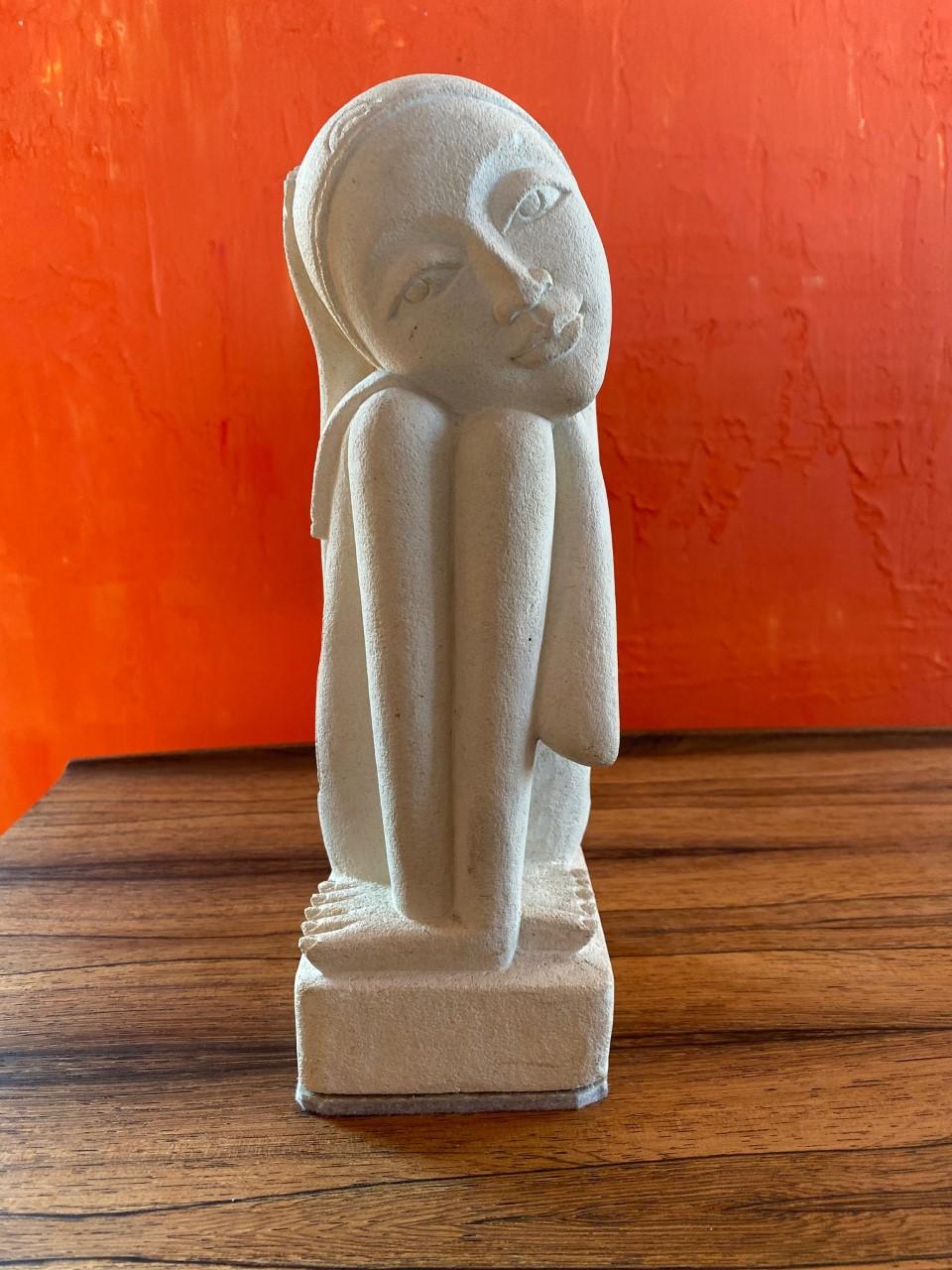Beautiful and enigmatic plaster sculpture of a sitting woman. This stylized rendering presents a female form that is long limbed but concentric around itself. The visage mesmerizes with big and delicate features. The head emulates a scarf-like motif