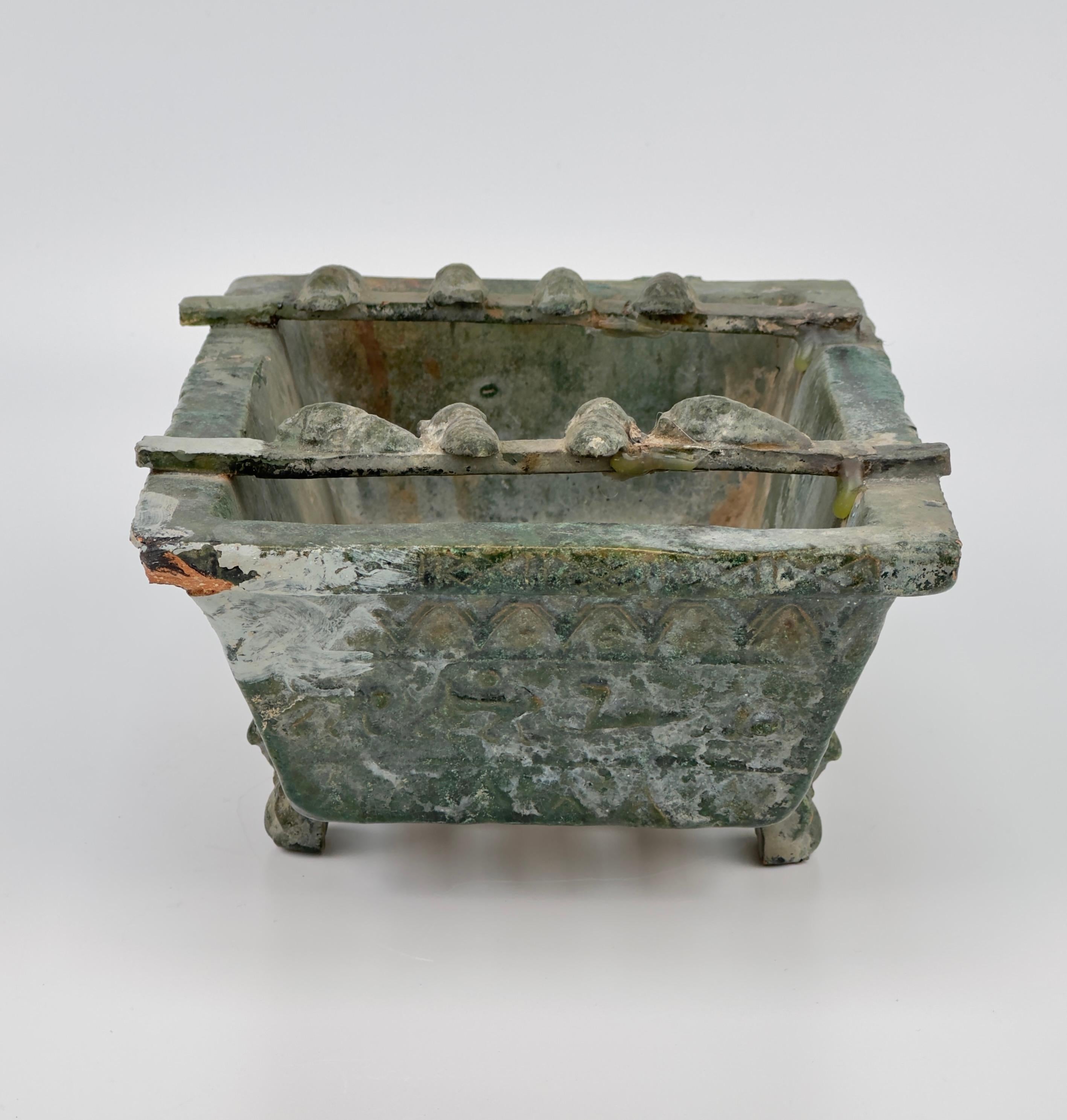 Ce brasero en poterie, un artefact funéraire de la dynastie Han, présente des côtés quadrilatéraux inclinés vers l'intérieur et une base avec des fentes d'aération. Chaque face est ornée de motifs animaliers et géométriques. Le brasero repose sur