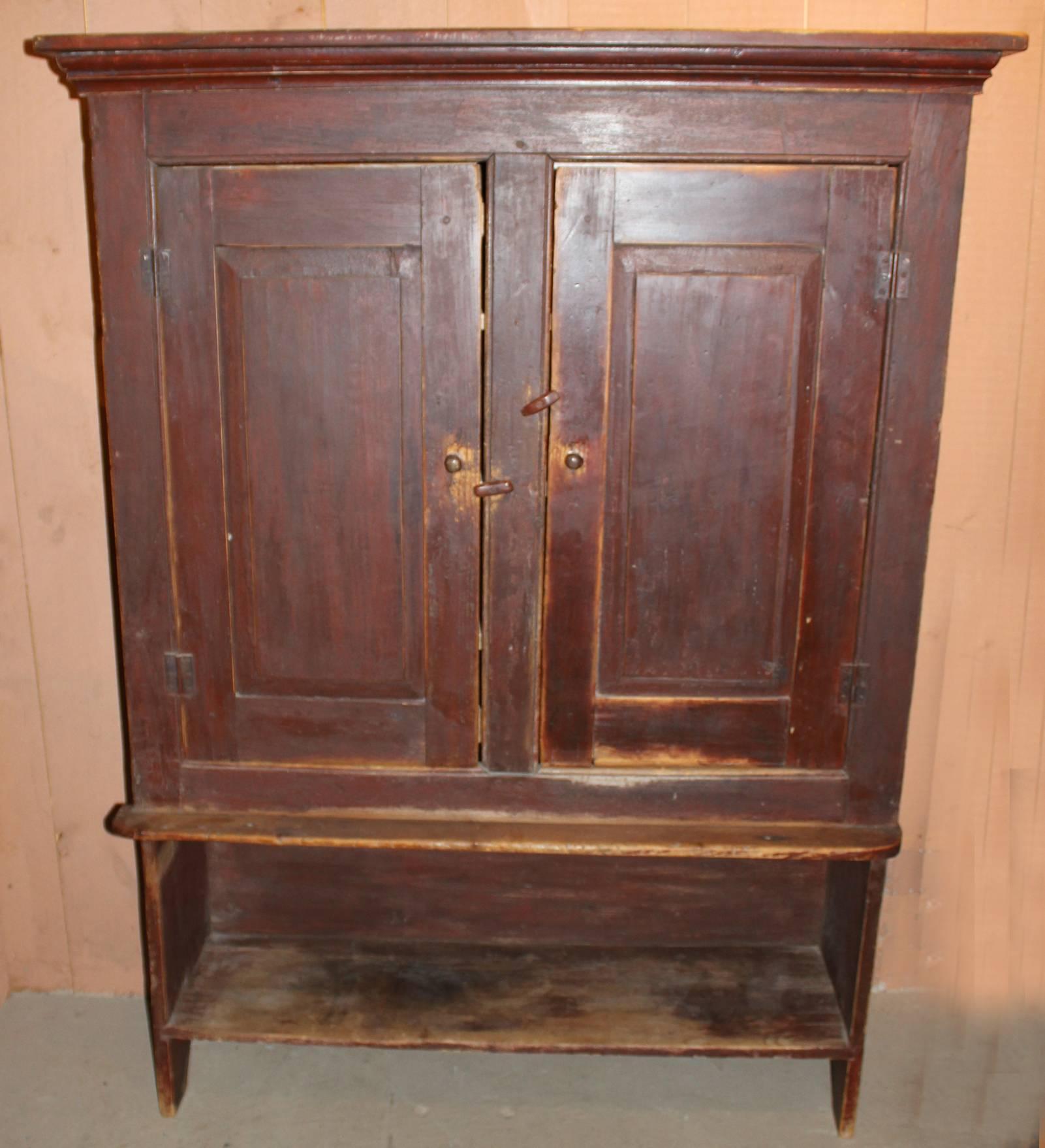 A rare form primitive pine hutch cupboard in old red finish, a molded cornice over two blind or paneled doors, opening to reveal three interior shelves, over an exposed lower shelf, with boot jack cutouts on each side. Dates to the early 19th