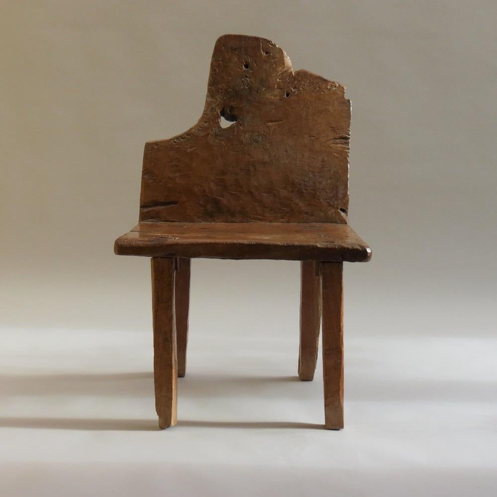 Ein seltener primitiver Stuhl mit ungewöhnlichem Design.  Sitz und Rückenlehne sind aus einem Stück Nussbaumholz gefertigt.  Die Beine werden durch den massiven Sitz gezapft und verkeilt, damit sie halten.  Auf dem ganzen Stuhl sind wunderbare