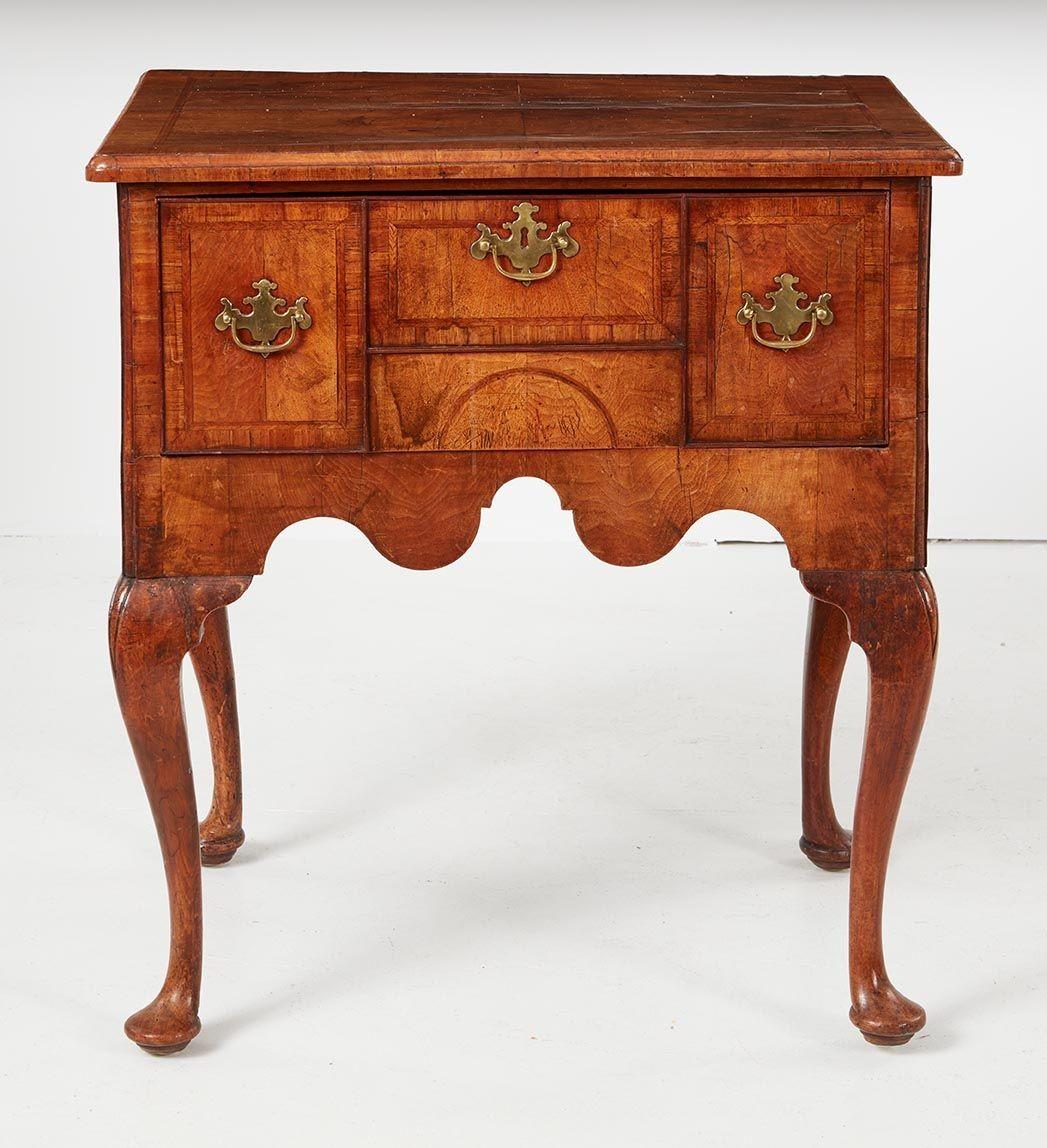 A rare and exceptional Queen Anne walnut lowboy, the quarter veneered figured walnut top with herringbone inlay and walnut crossbanding over one deep drawer constructed to resemble three drawers, over scalloped apron and standing on cabriole legs,