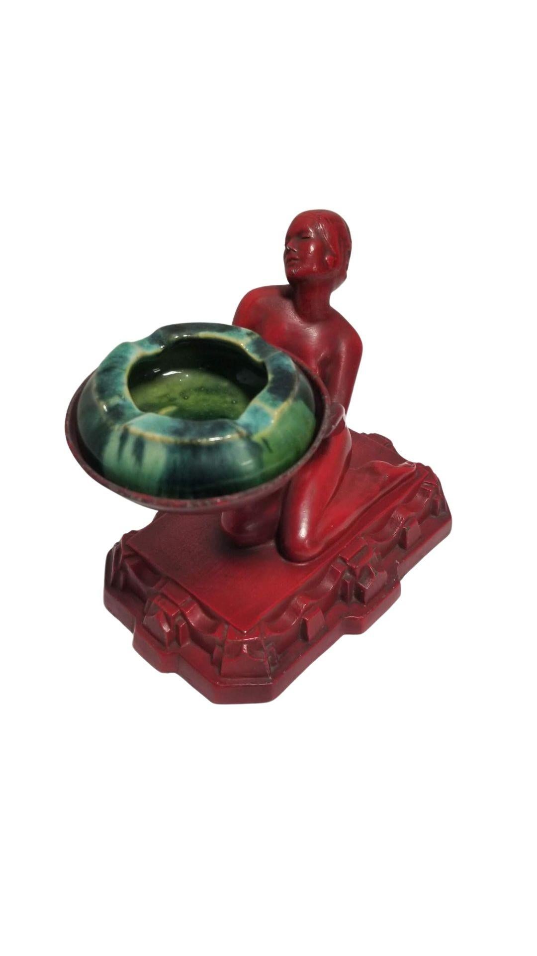 1920s Art Deco ashtray or ring holder by Nuart featuring a nude female figurine offering an ashtray in an oriental red finish with green ceramic Brush McCoy pottery ashtray.

Nuart specialized in crafting decorative household items in the Art Deco
