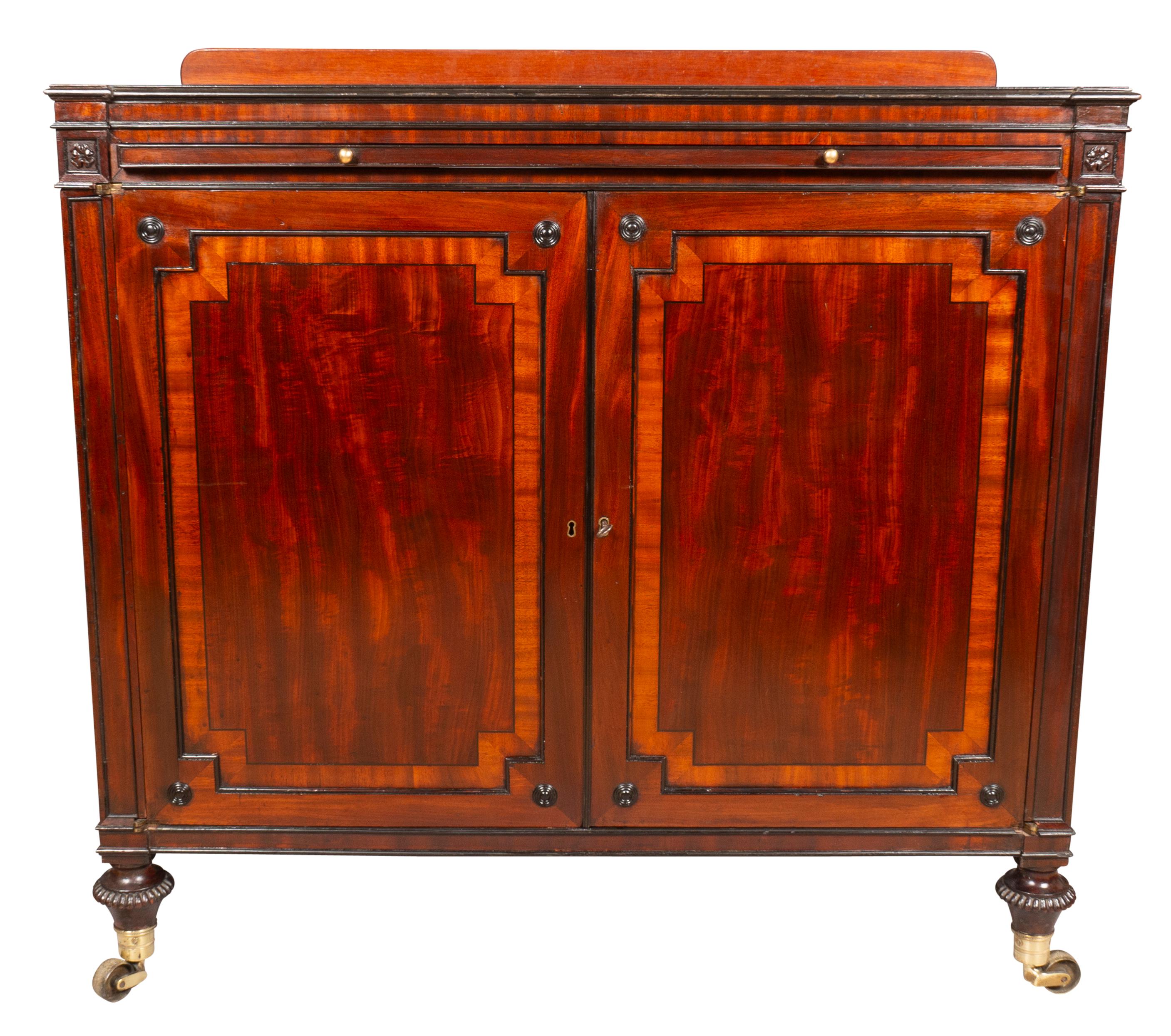 A finely crafted piece with a rectangular top with leather inset and ratcheting book stand over a brushing slide over a pair of paneled doors enclosing sliding tray shelves. The back is finished like front with false doors. Sides have brass ring