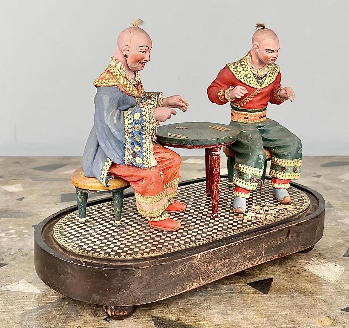 A rare Regency polychrome painted pottery diorama of two Chinoiserie card-players, shown in traditional dress and with nodding heads seated at a circular table with cards also strewn across the checkered floor. The left hand figure nodding his head