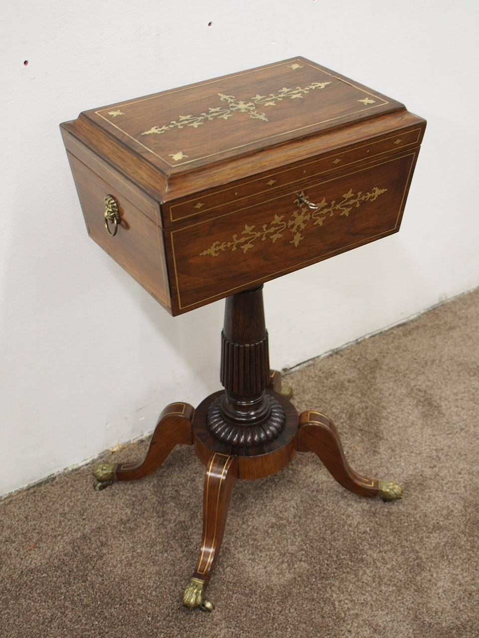 Rare Regency rosewood and brass inlaid teapoy on stand, circa 1815. The sarcophagus shaped teapoy has brass beading and an elaborate brass pattern to the centre and brass inlaid front. To the sides are cast brass lion mask head with pull rings. It