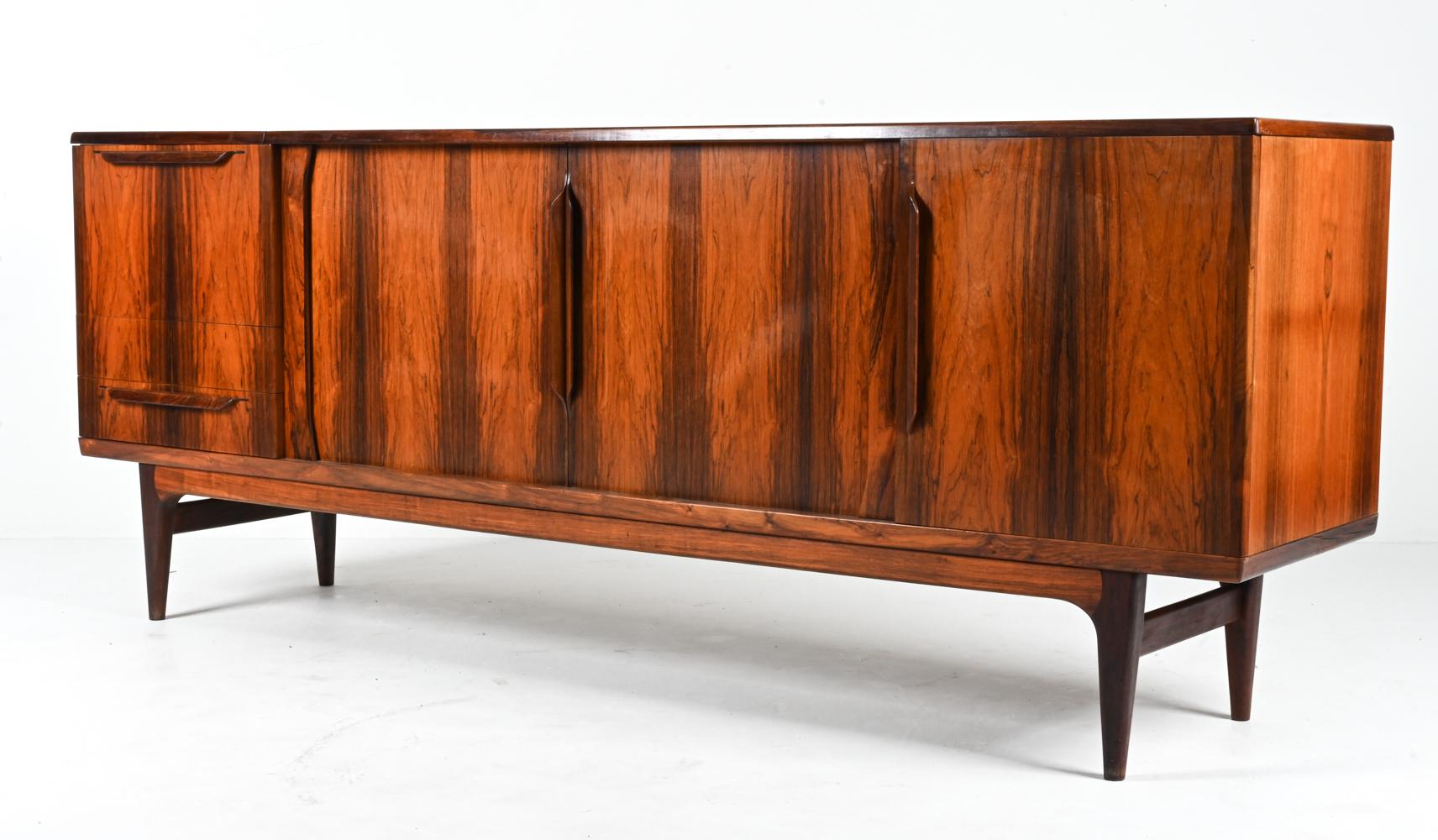 Designed by the inimitable Johannes Andersen, this exceptional Danish Mid-Century sideboard features not only luxurious bookmatched rosewood veneers, but also a rare configuration that's full of surprises and features. 

The central tambour doors