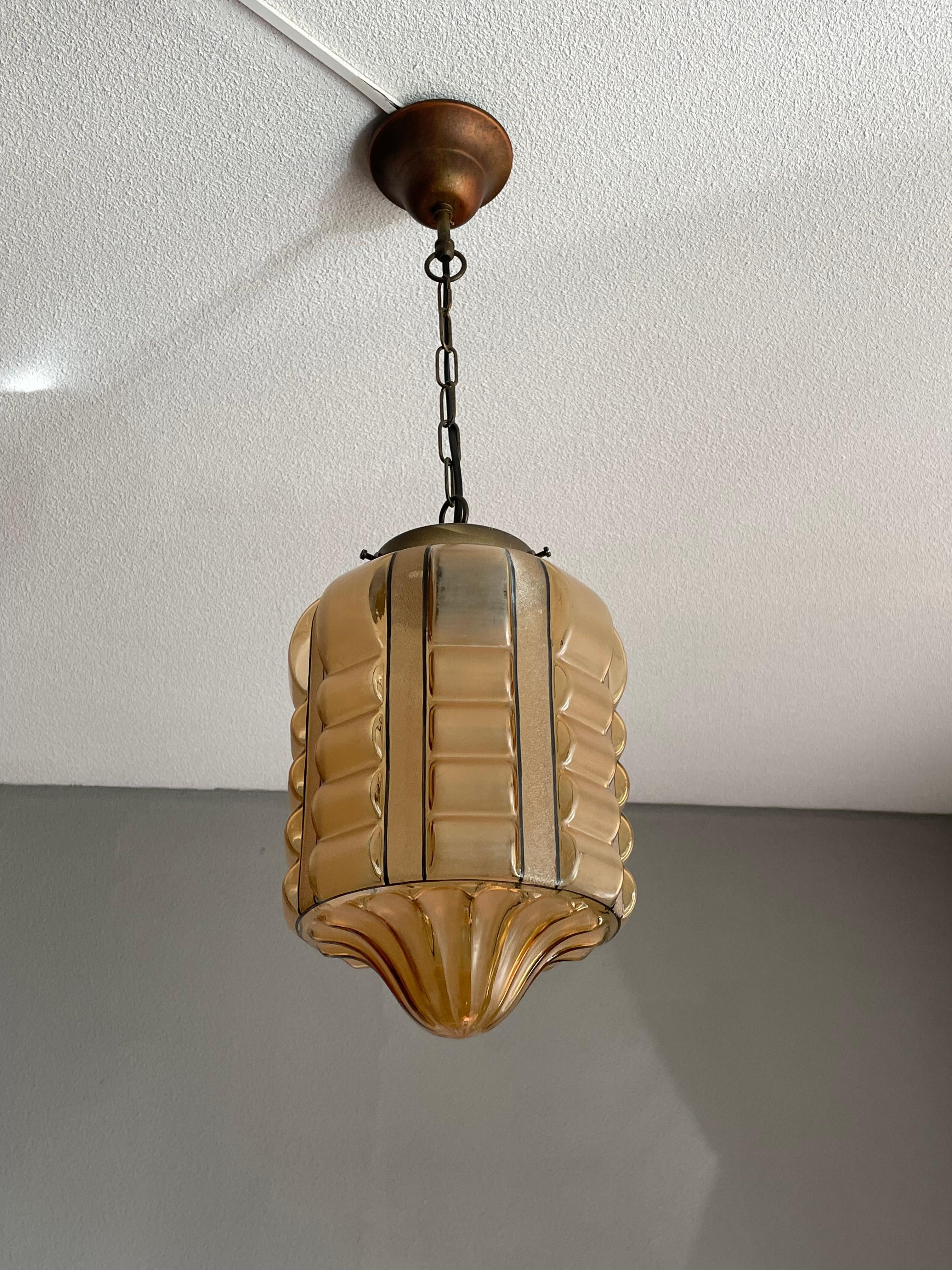 Beautiful shape and great amber color Art Deco hallway pendant.

This rare Art Deco glass pendant with its wonderful colors and striking, geometrical design could be the perfect light fixture for your entrance or bedroom. The warm light that it