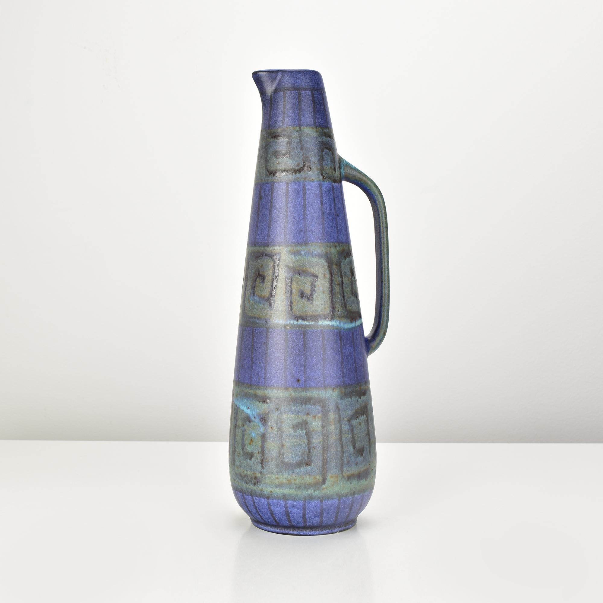 This striking mid-century modern handled jug vase is a rare piece from the Hellas series by Ruscha Keramik, Germany. Crafted in ceramic, the vase showcases a bold, tapered silhouette with an angular handle and a pronounced spout. It features a