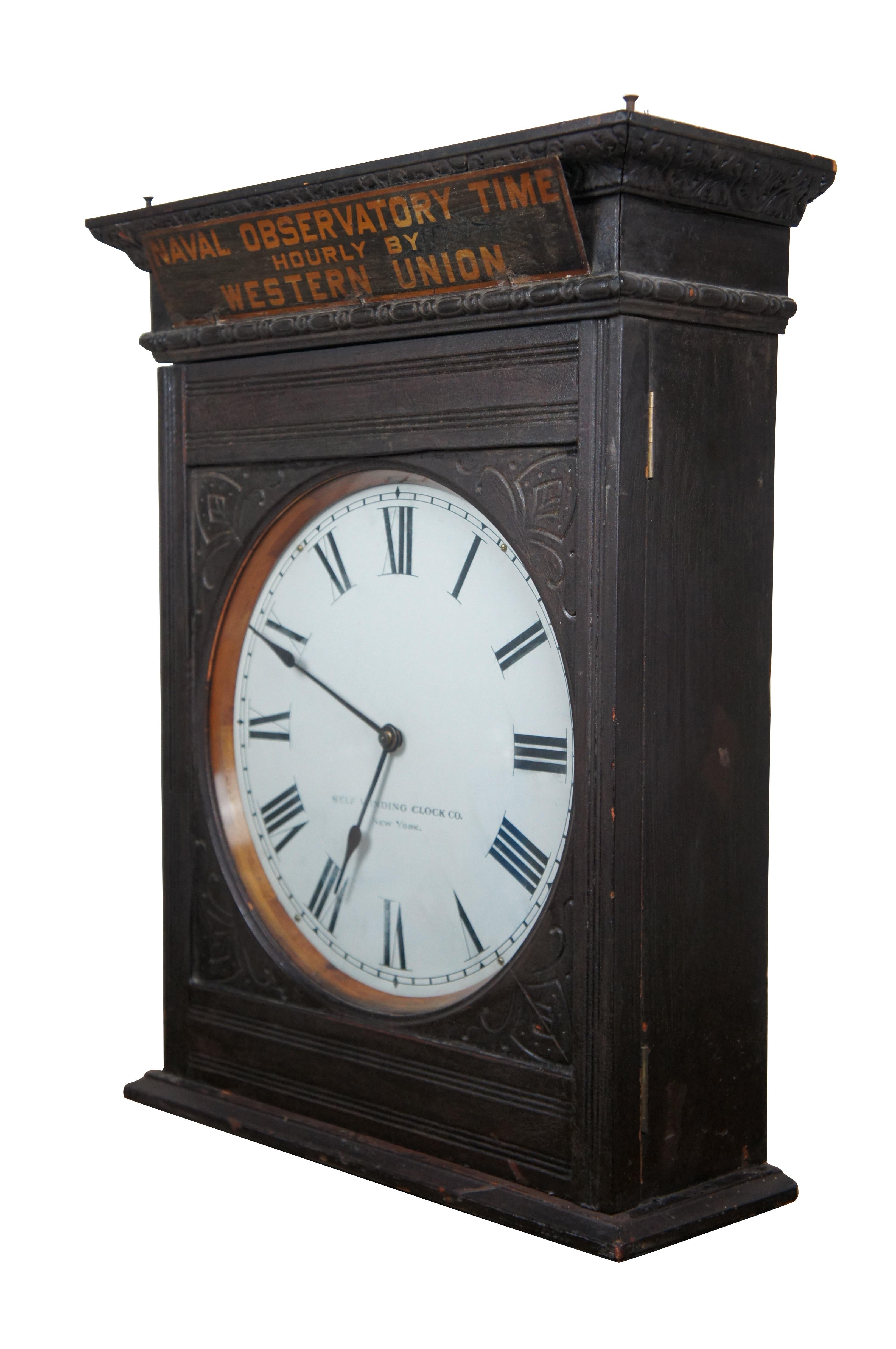 Antique Western Union, Naval Observatory Time, self winding clock. Features a tall wooden case with carved corners and pediment mounted with tin sign reading 