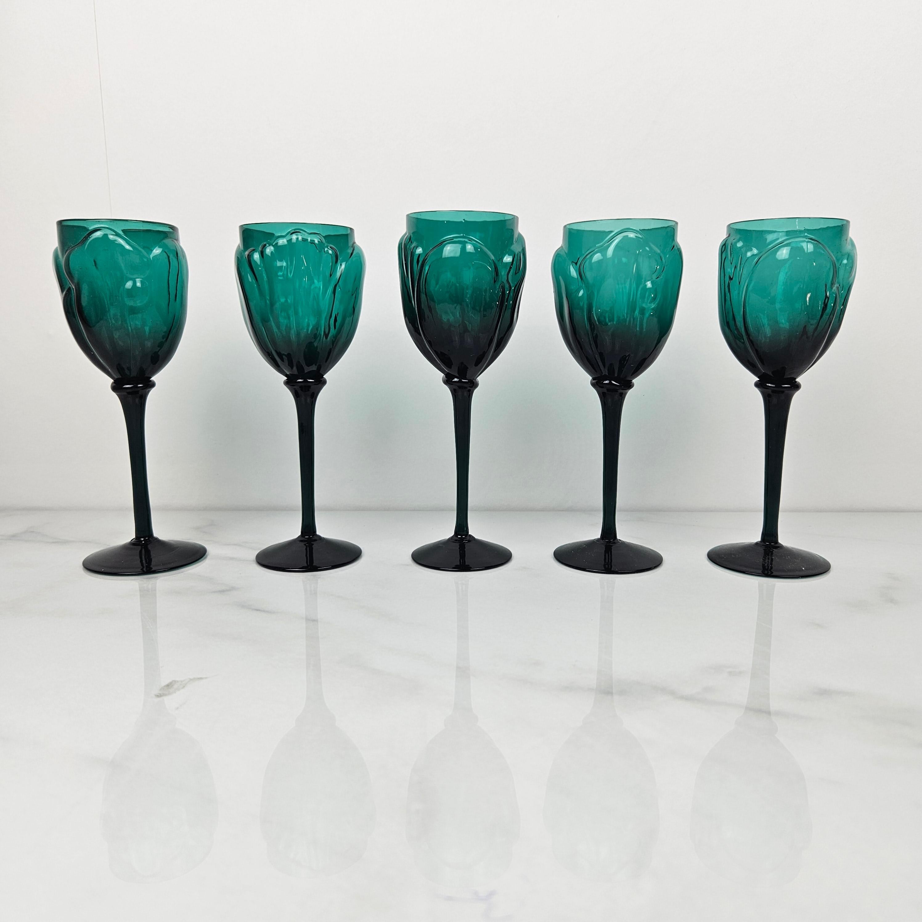 An exceptionally rare and elegant set of five hand-blown wine glasses from the 1920s, showcasing the refined artistry of the Art Deco era. 
Crafted in a rich emerald green hue, each glass features a delicately raised floral or petal motif around the